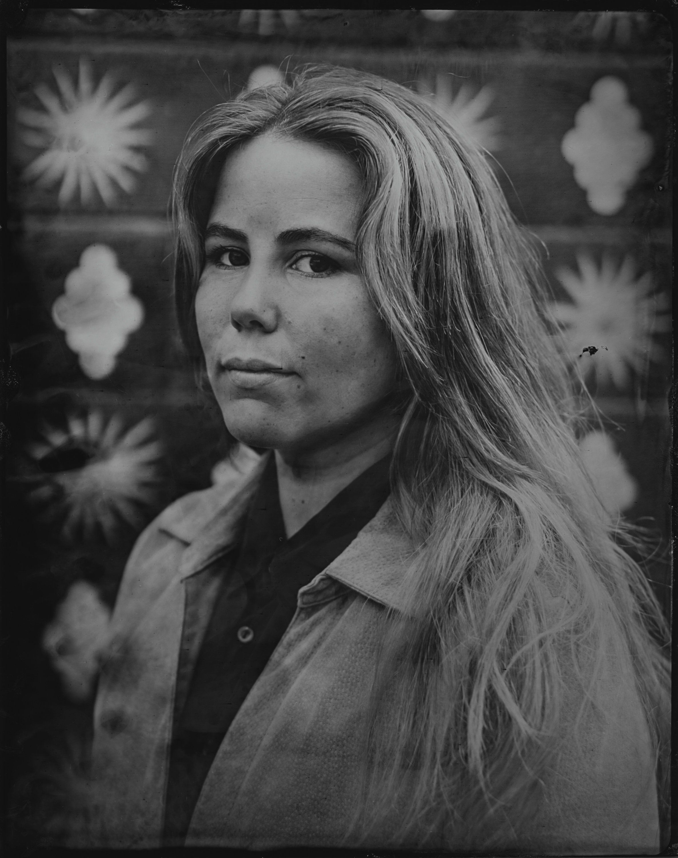 Woman with long hair in profile, wearing collared shirt against patterned background of geometric shapes and light bursts in black and white tintype style