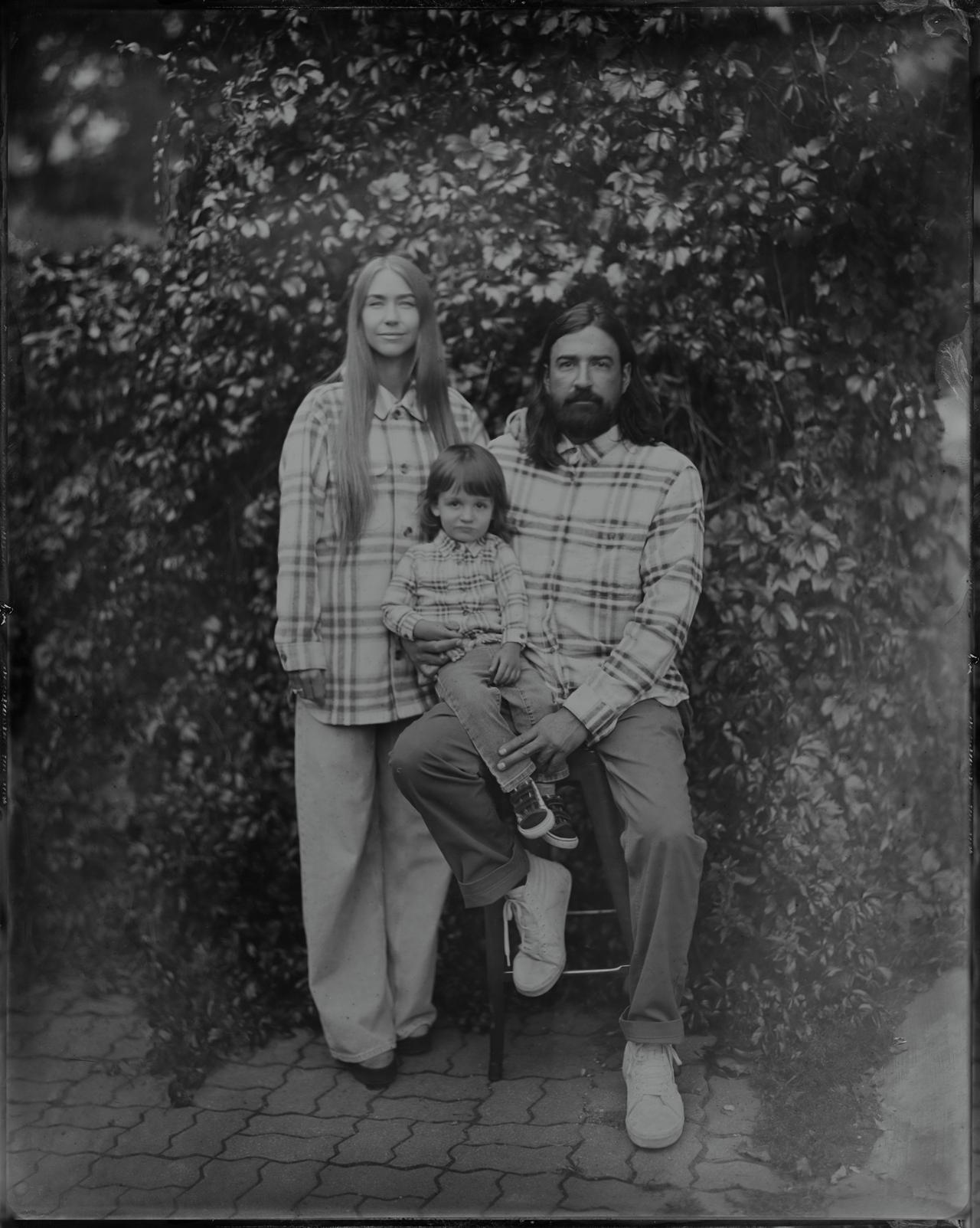 Father holding young child with mother beside them, posed against foliage in tintype portrait