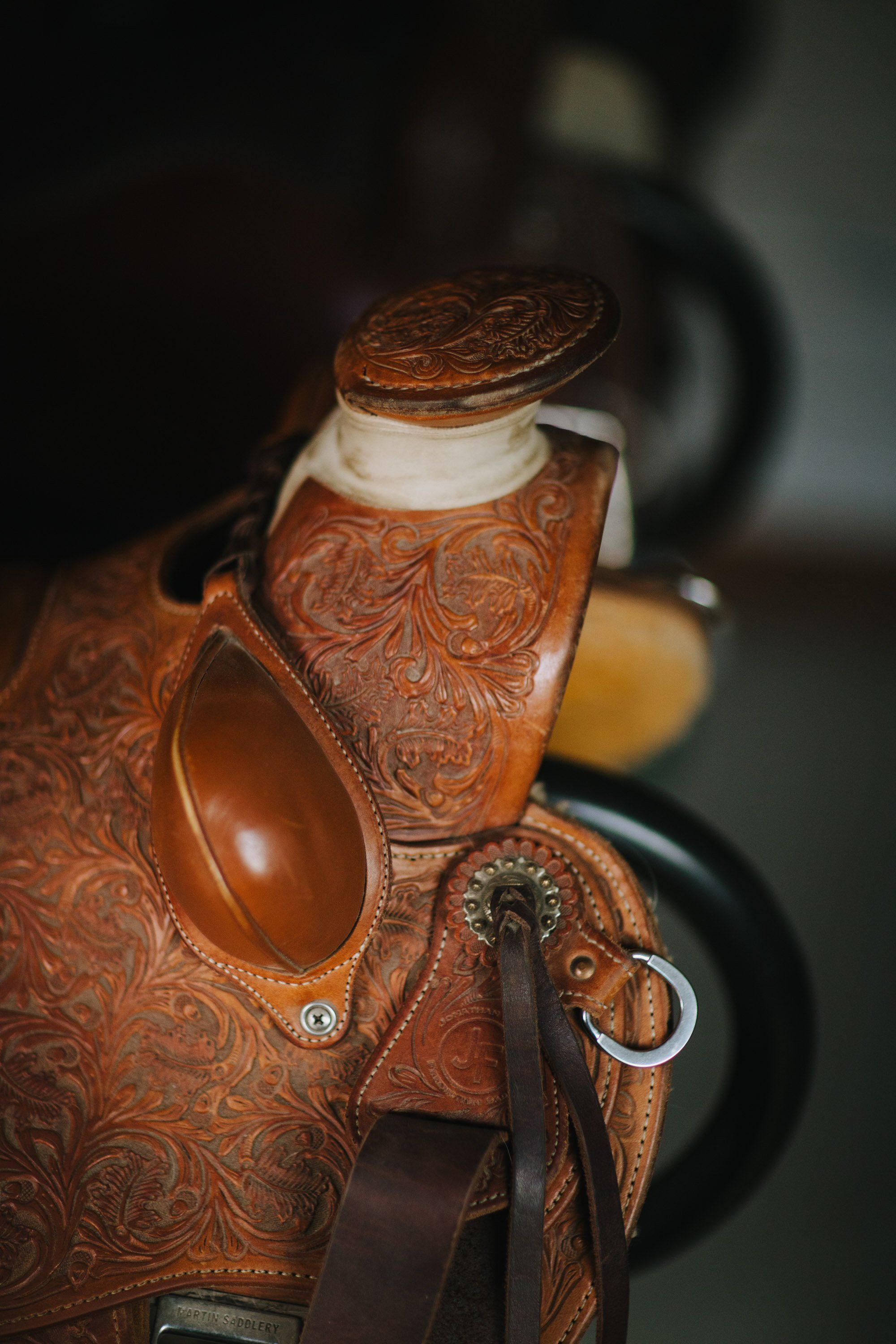 Intricately tooled leather saddle with ornate floral patterns catches warm light against a blurred dark background
