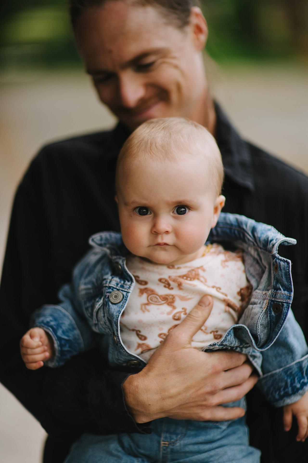 A bearded man holds a fair-haired infant, both gazing downward with serene, contemplative expressions