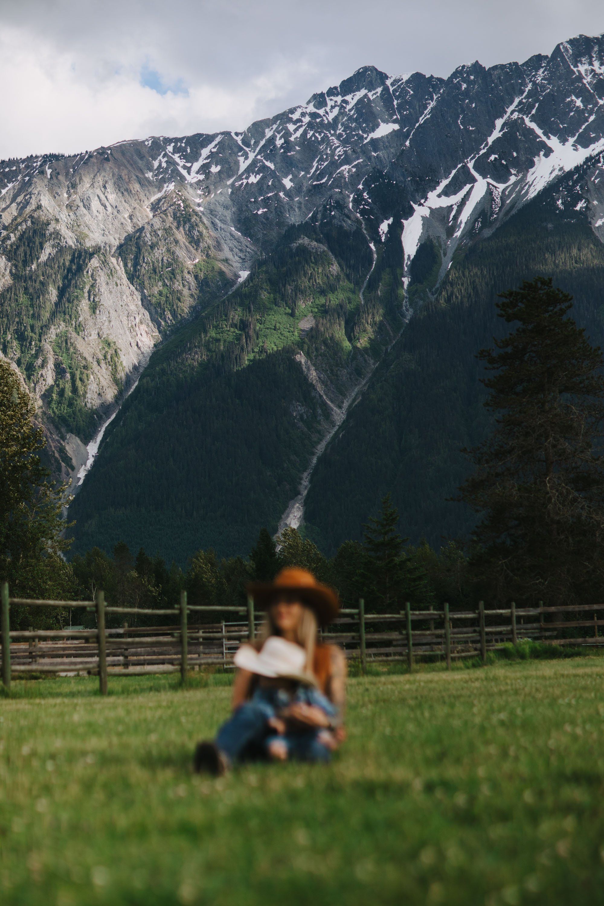 Blurred figure of child playing in green meadow with snow-capped mountains and forested valley in sharp focus behind