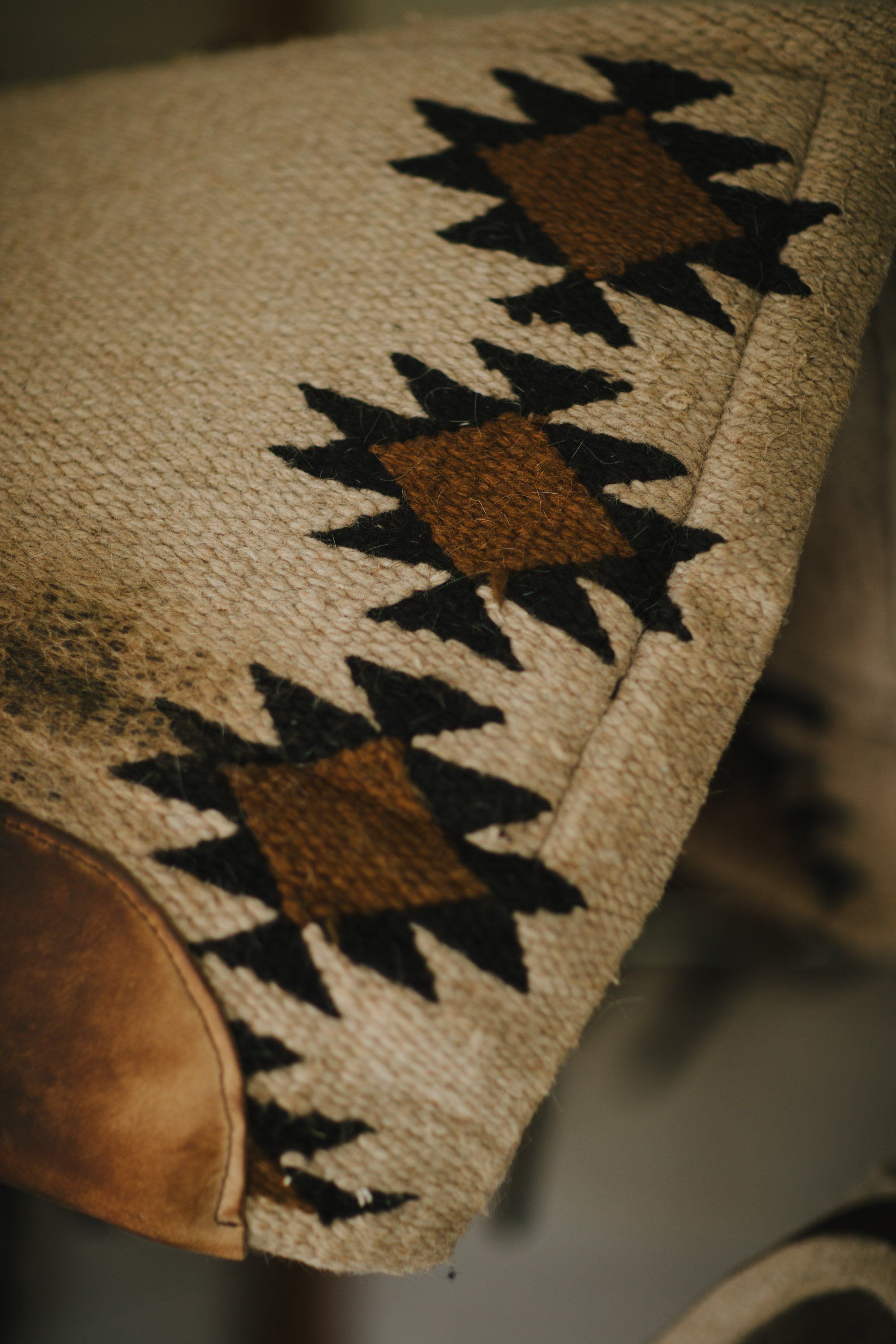 Close-up of a cream linen garment with brown leather elbow patch and geometric black tribal-inspired pattern