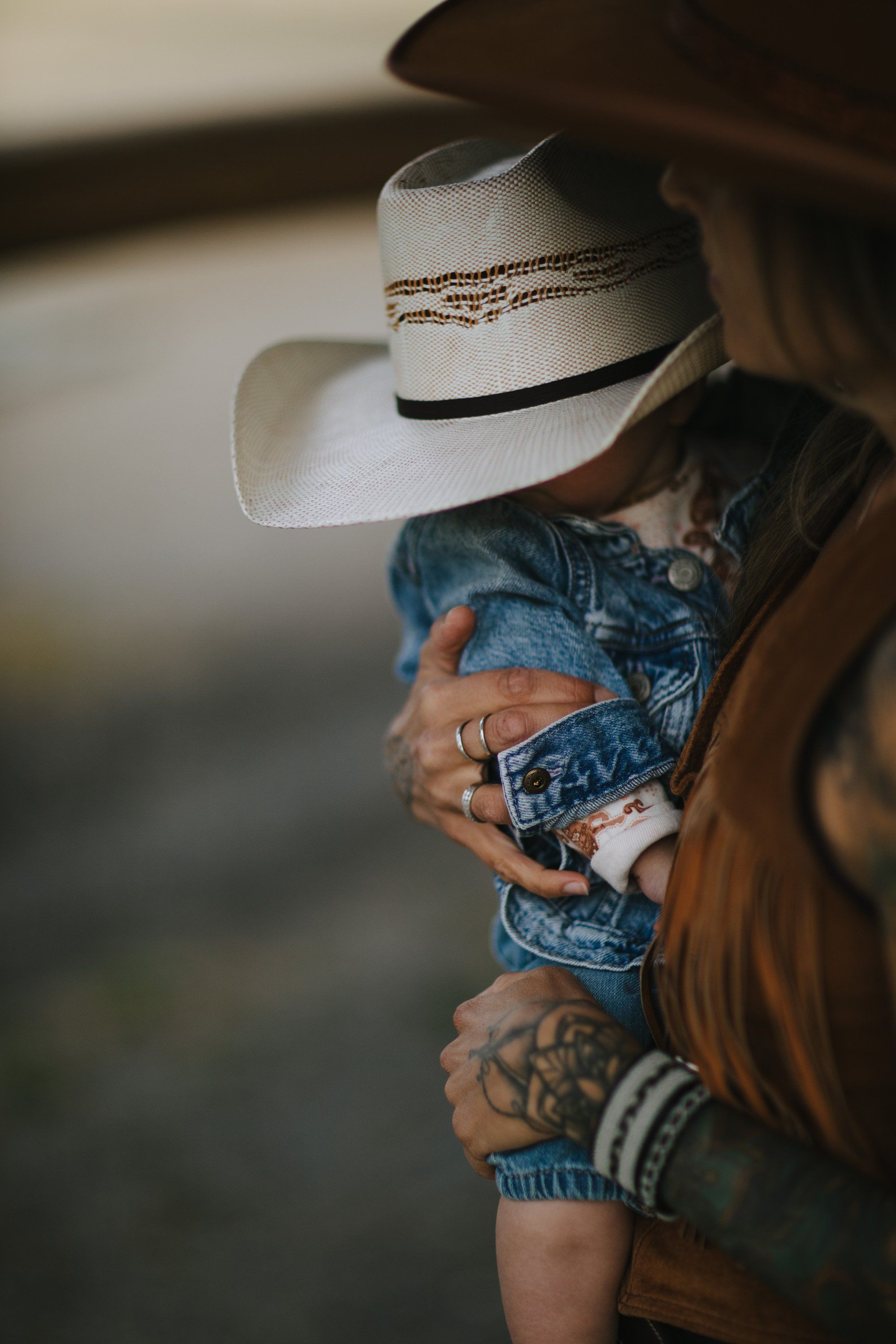 Parent in cowboy hat and denim holds child against warm, blurred backdrop in golden afternoon light