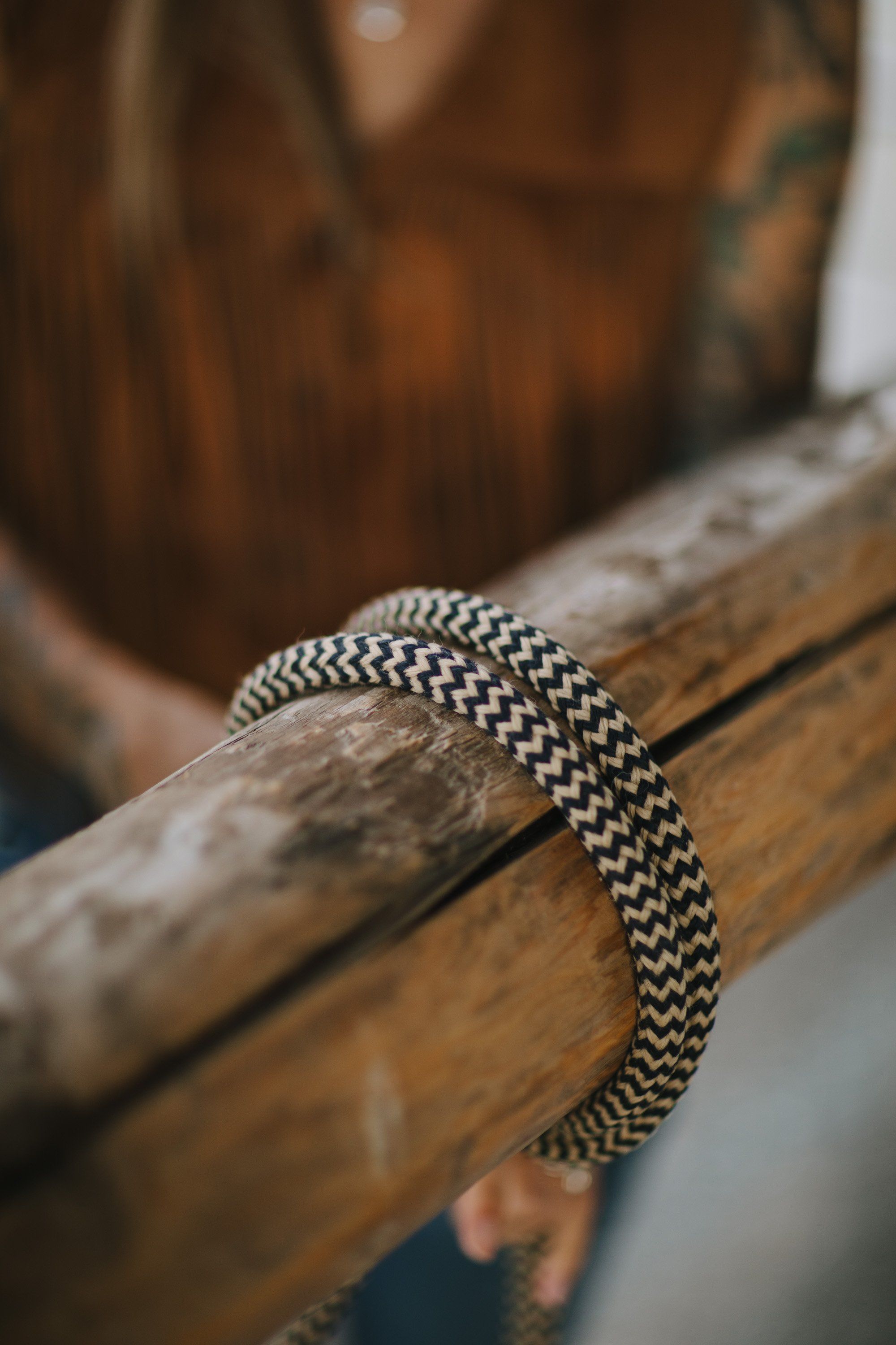 Close-up of a woven silver bracelet on a weathered wooden branch, warm earth tones blurred behind