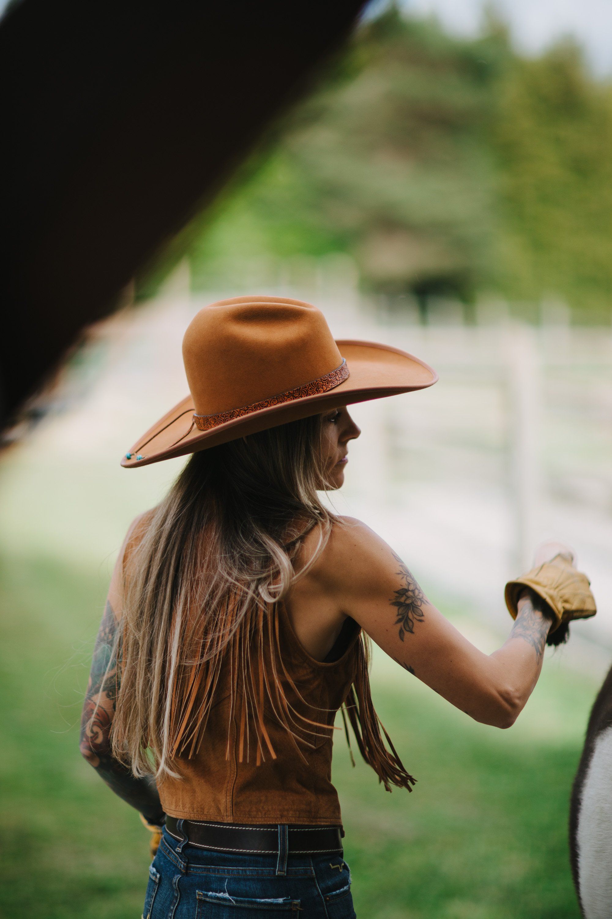 Woman in brown cowboy hat and fringe vest holds a young child, backlit by green landscape in Pemberton