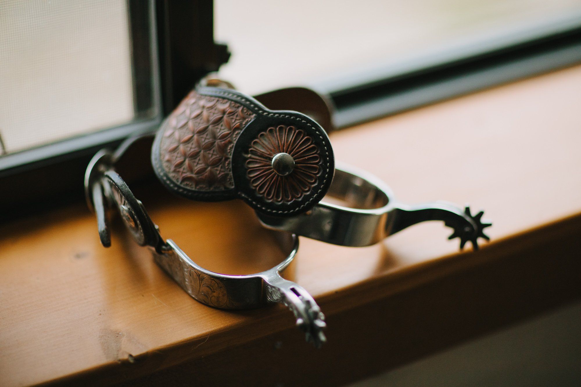 Ornate silver jewelry with textured stones and spurs arranged on warm wood, backlit by window light