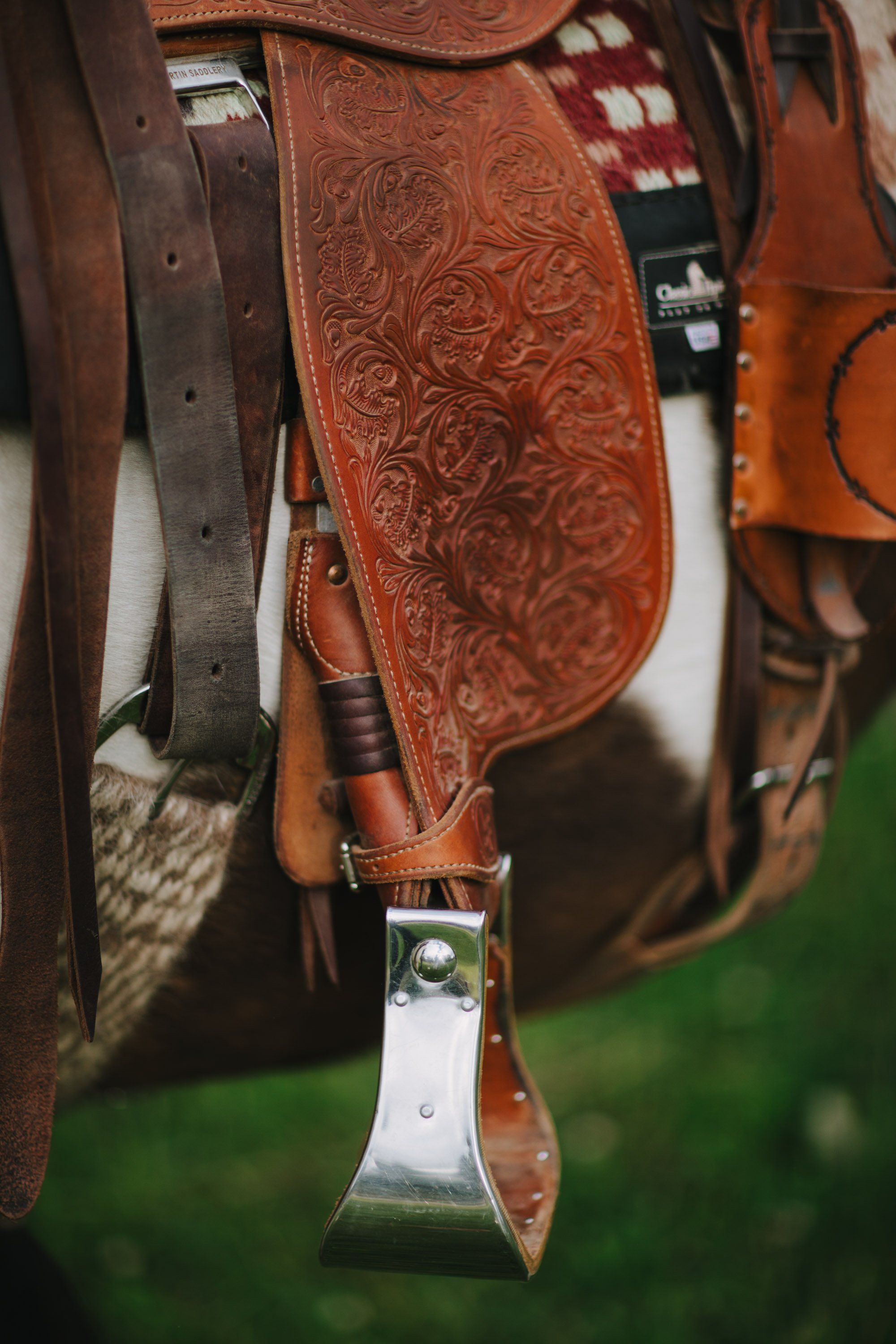 Ornate tooled leather saddle with silver stirrup and blanket, close-up detail shot