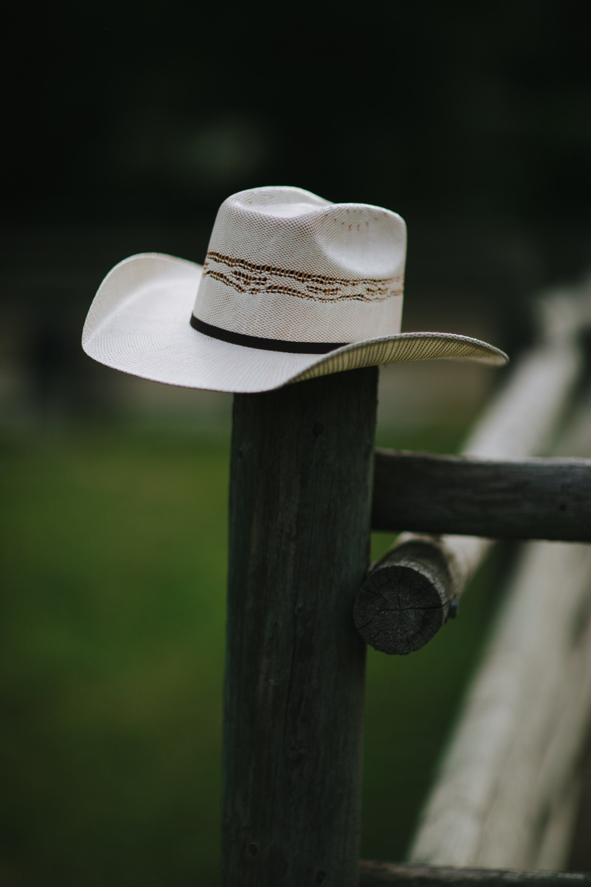 White cowboy hat hanging on a weathered black fence post with soft green background
