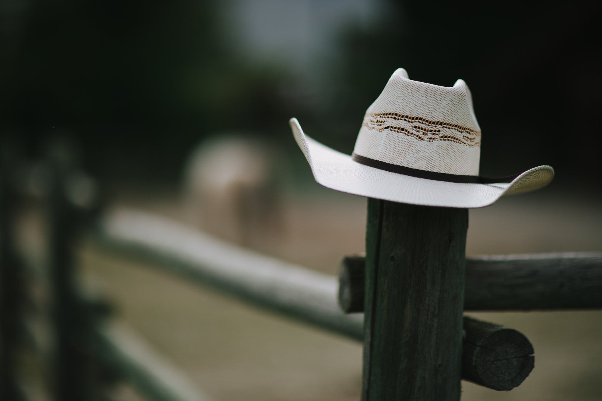 White cowboy hat perched on wooden fence post with blurred ranch landscape behind