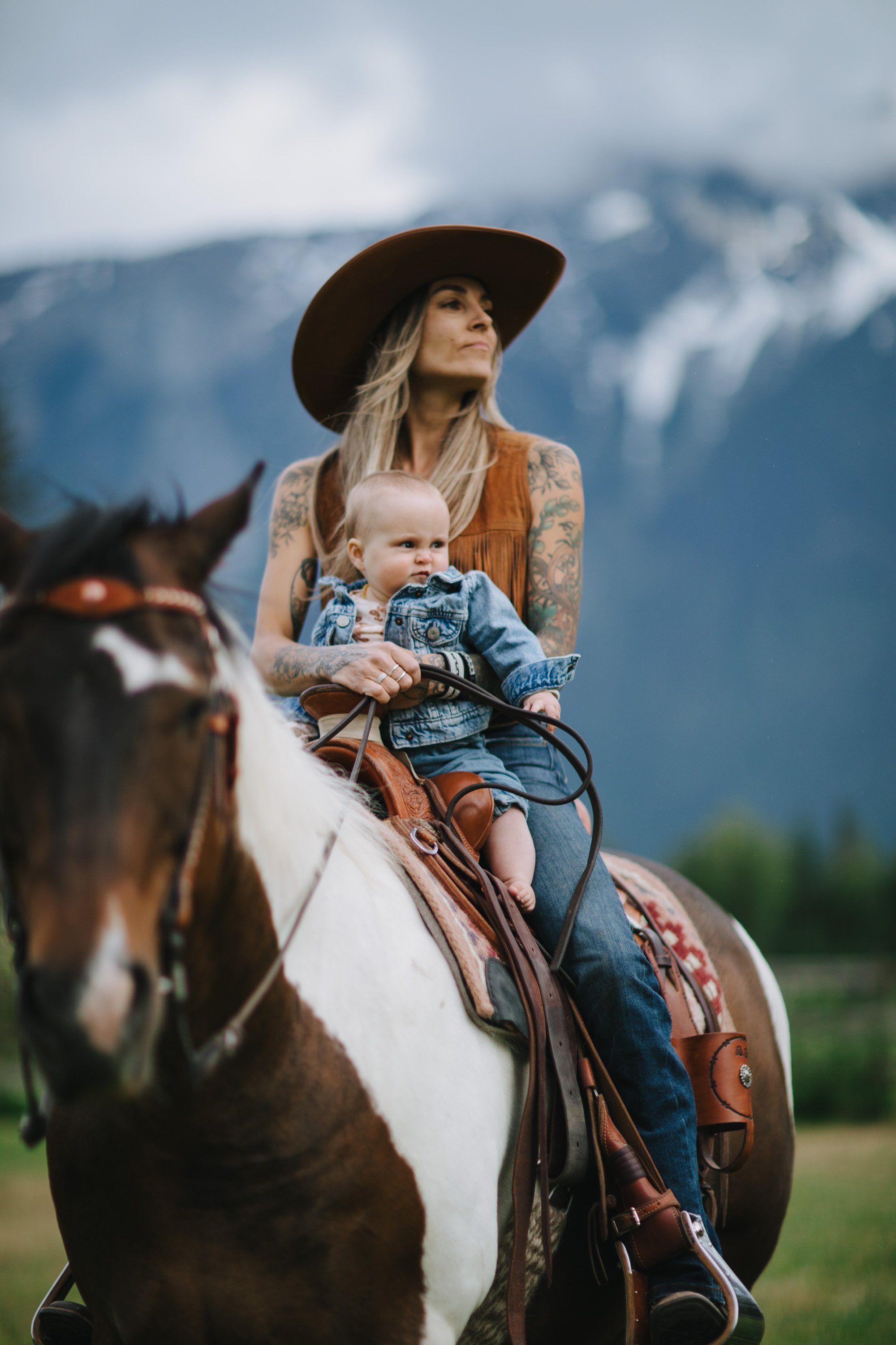 Woman and young child on horseback against misty mountain backdrop in pastoral valley setting