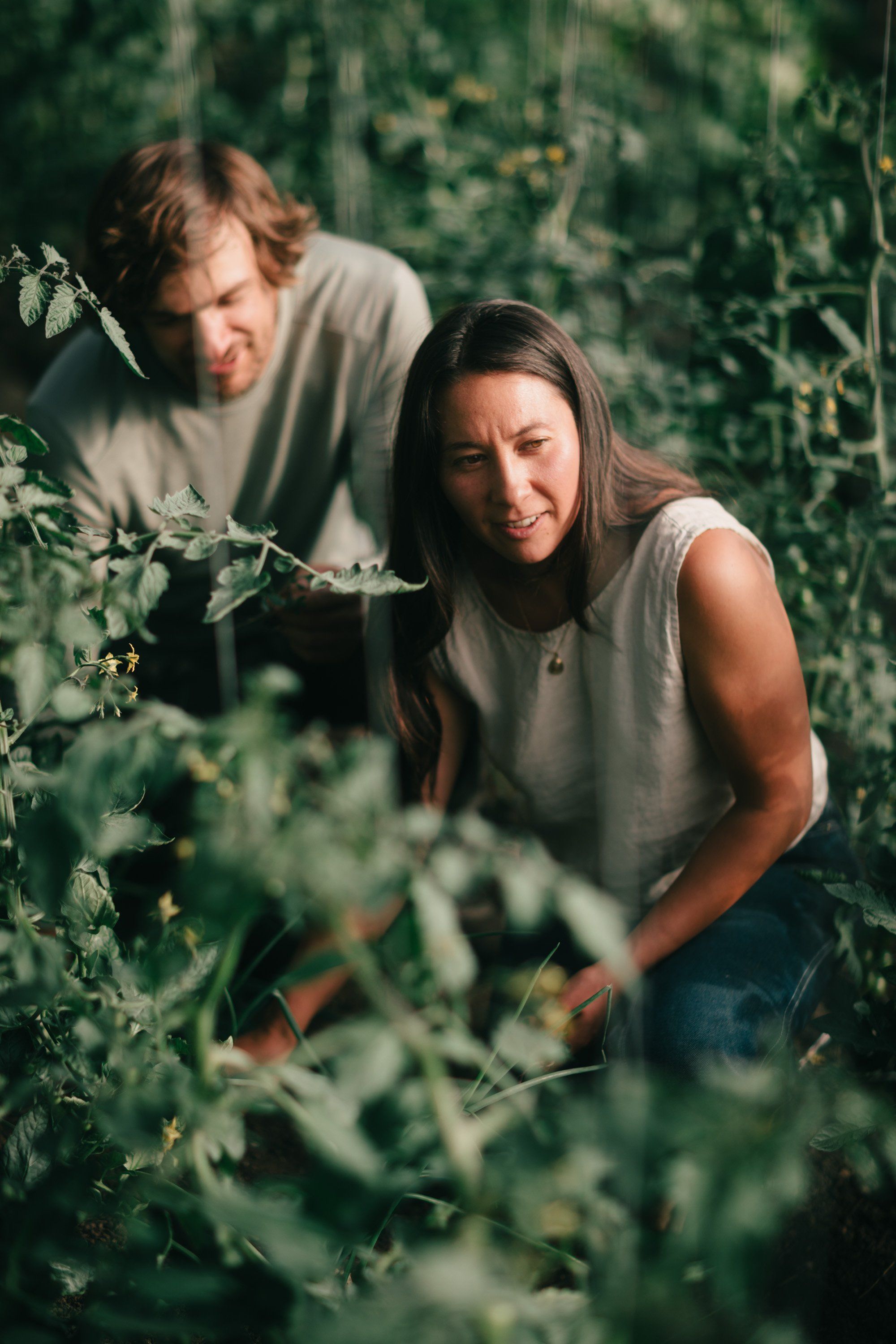 Couple nestled among lush green foliage on a farm, soft natural light filtering through leaves, intimate and serene woodland setting