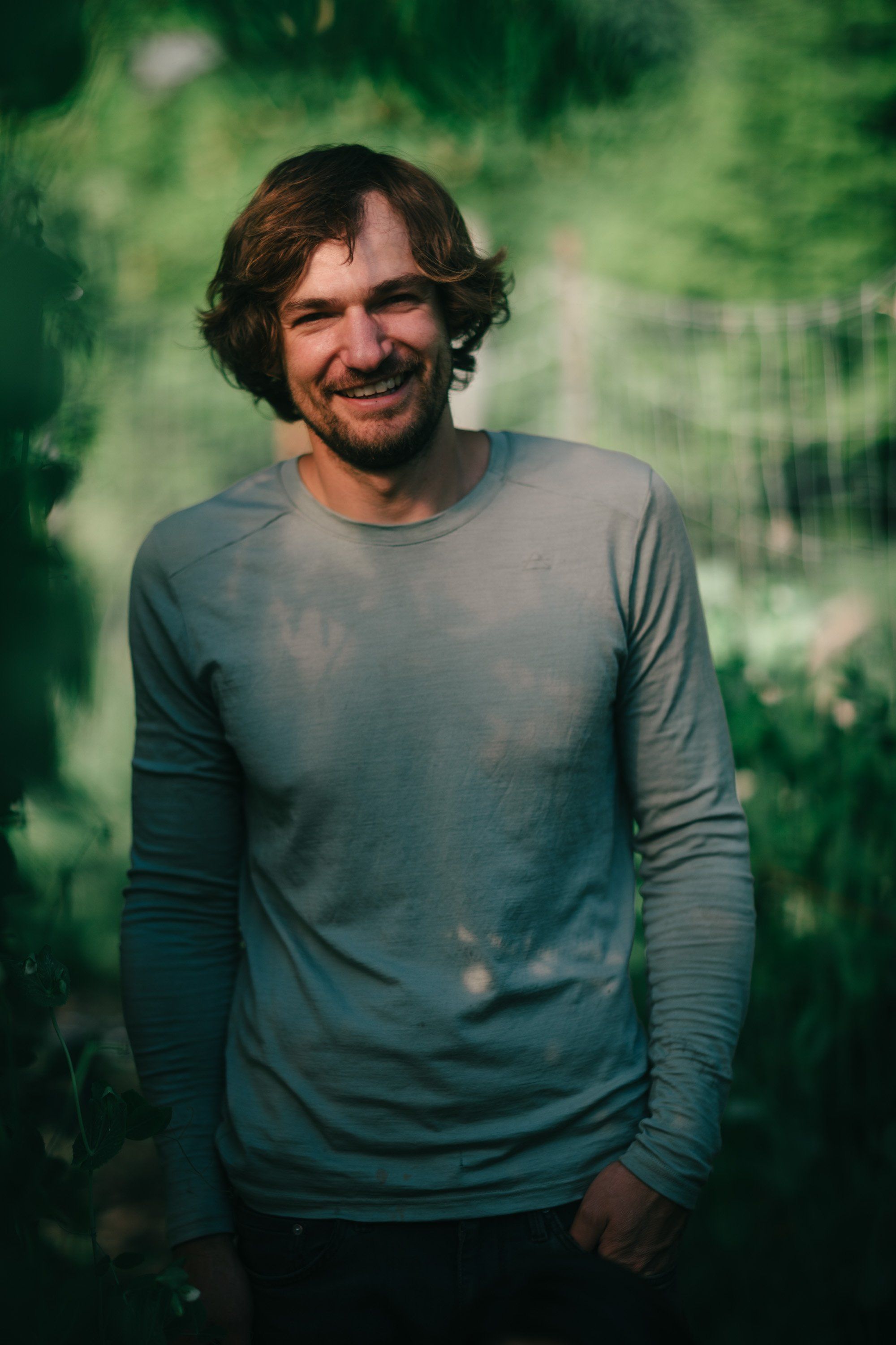 Man in blue-green long-sleeve shirt smiling at camera with soft-focused forest backdrop on Salt Spring Island