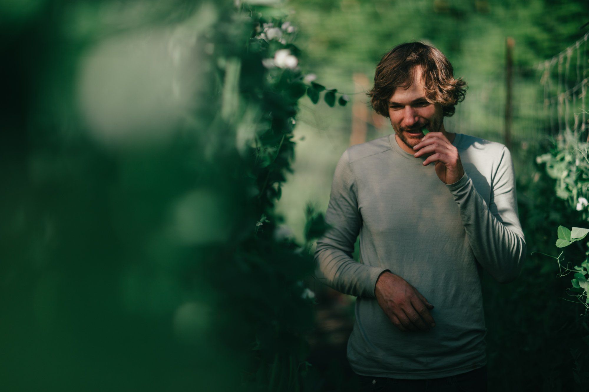 Man in light sweater surrounded by lush green foliage and vines in dappled forest light