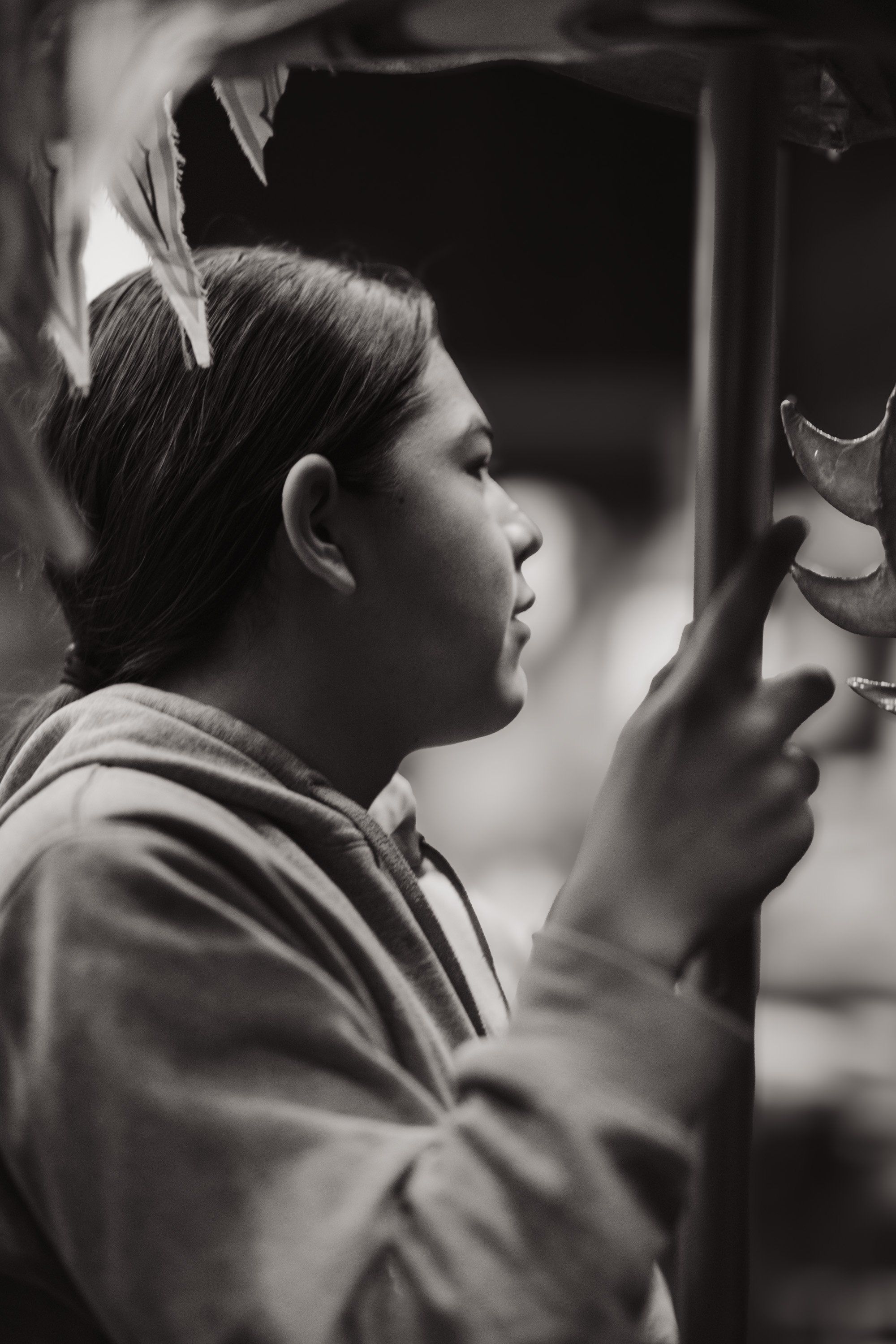 Young person in profile gazes at a carved wooden mask, soft window light illuminating their contemplative expression