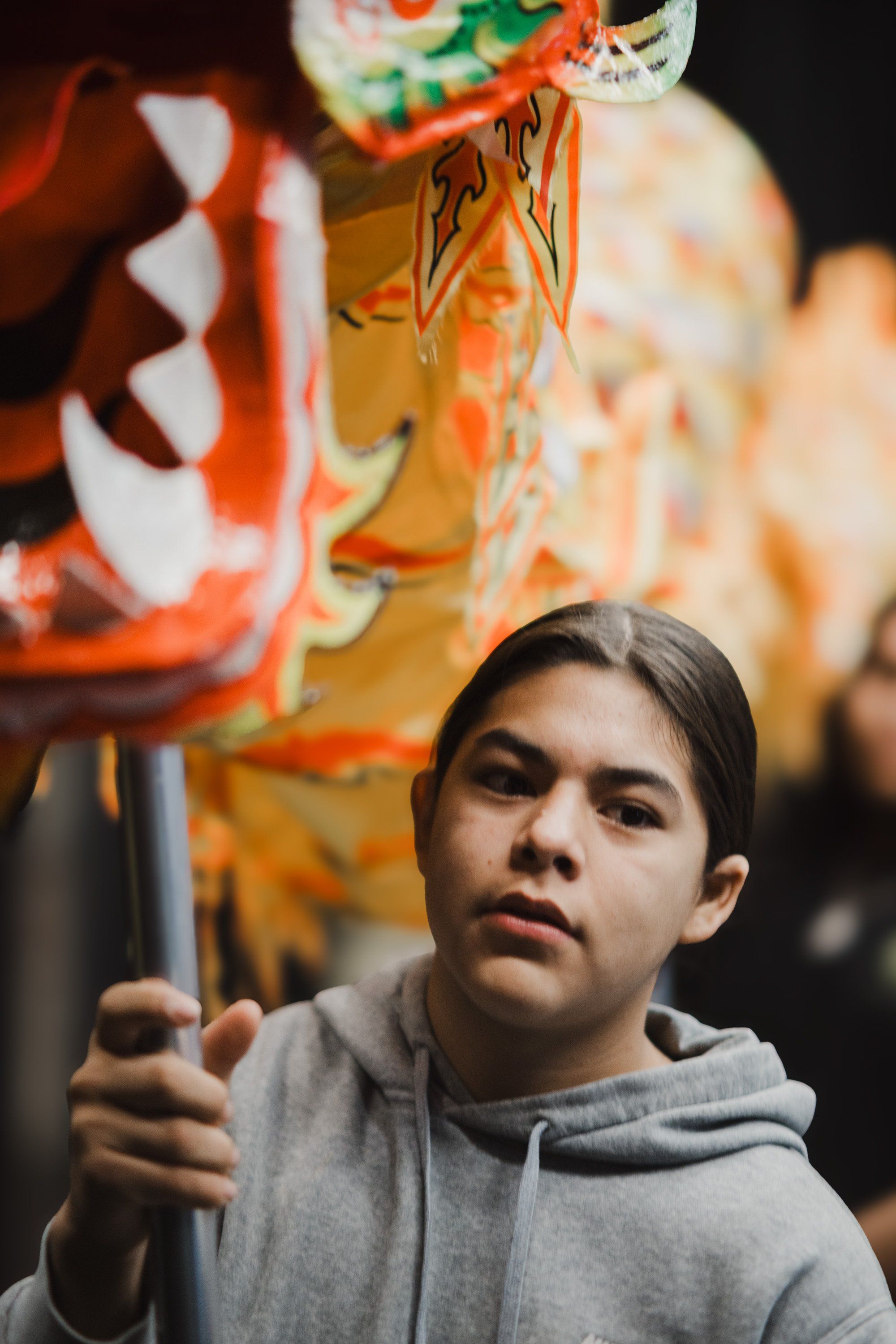 Young person in grey hoodie gazes upward at illuminated Coast Salish art installation with warm orange and traditional design elements