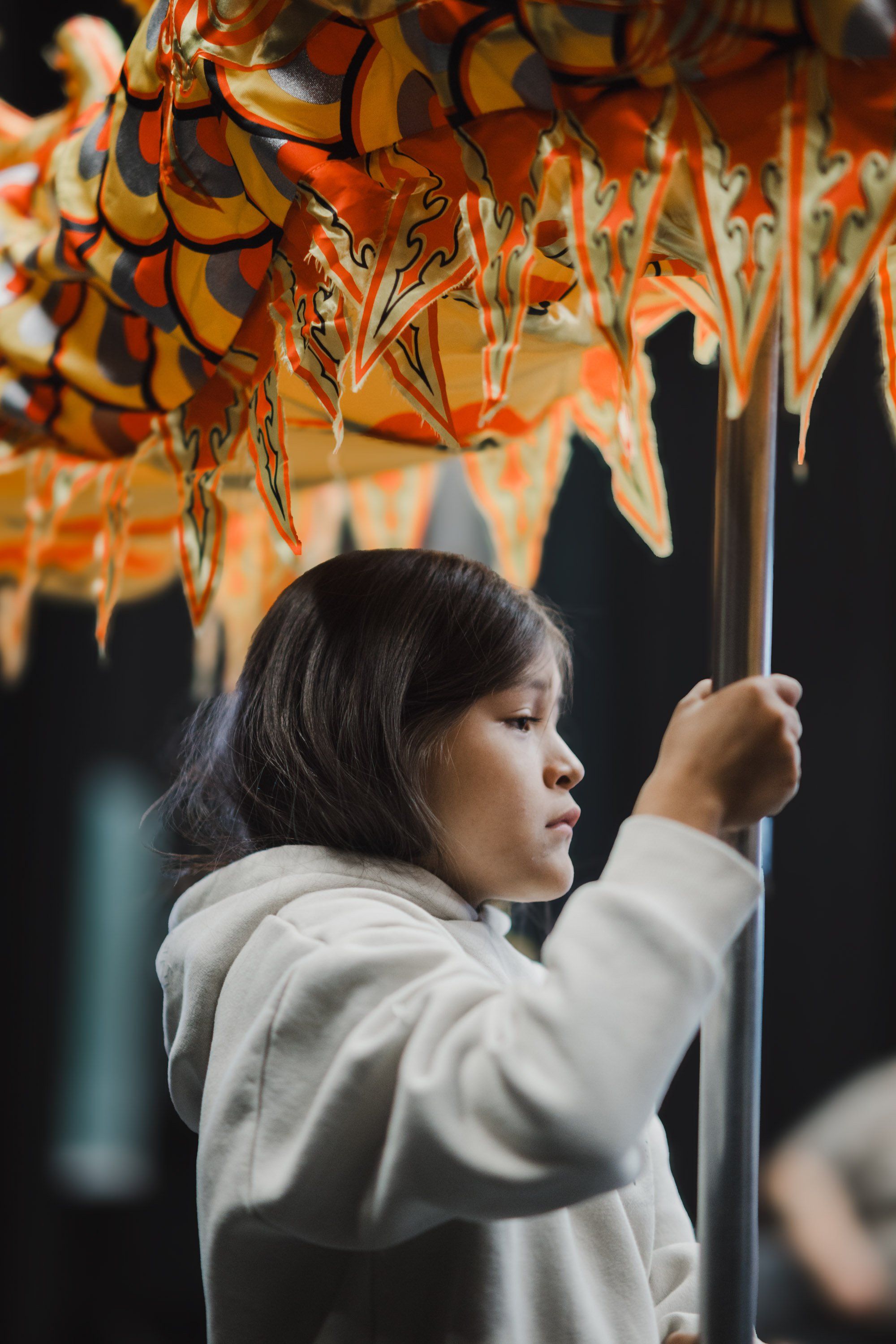 Young woman in profile reaching toward orange and black geometric patterns hanging above, soft natural light illuminating her thoughtful expression