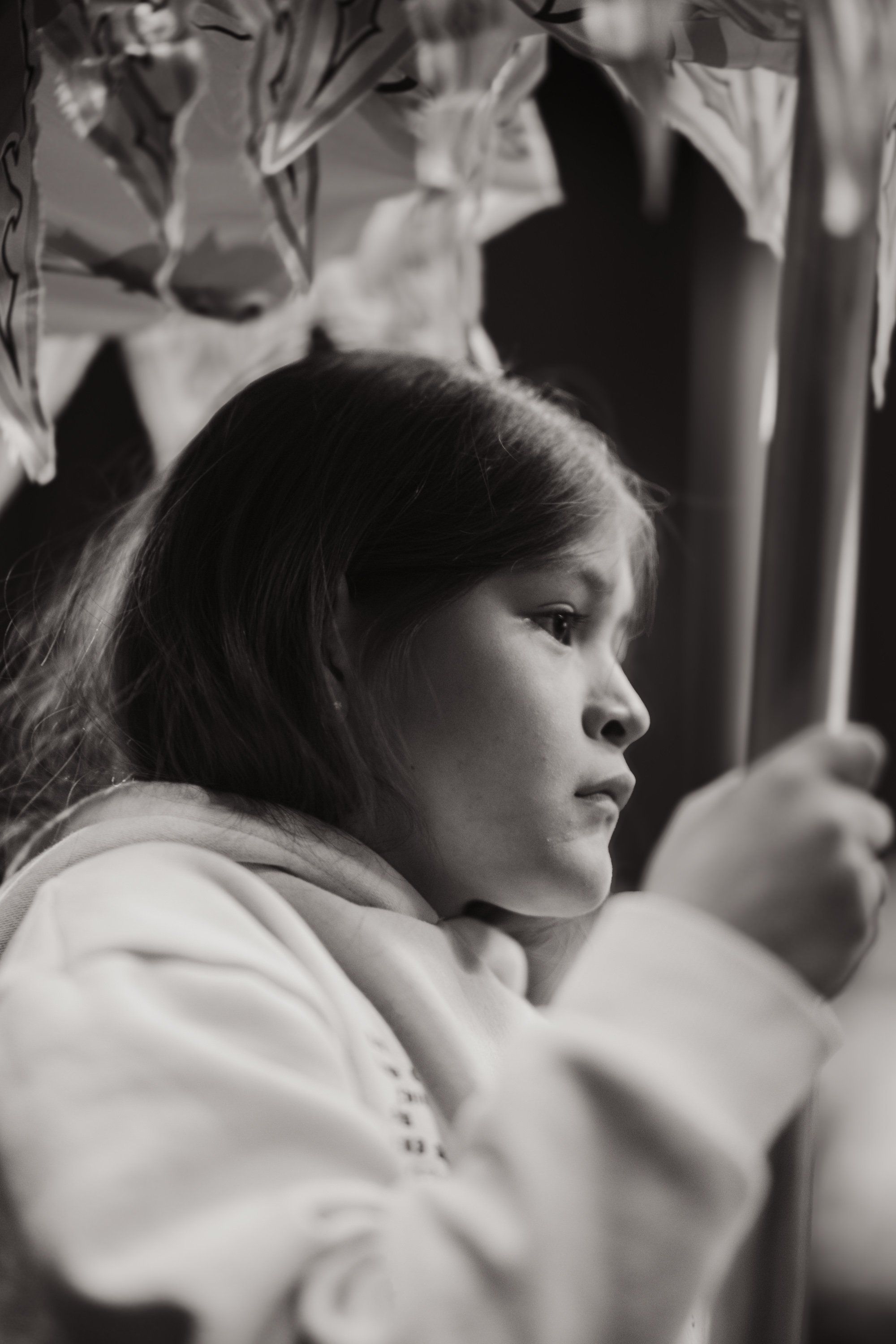 Young person in profile, gazing thoughtfully aside in soft natural light, wearing a light-colored garment against blurred background