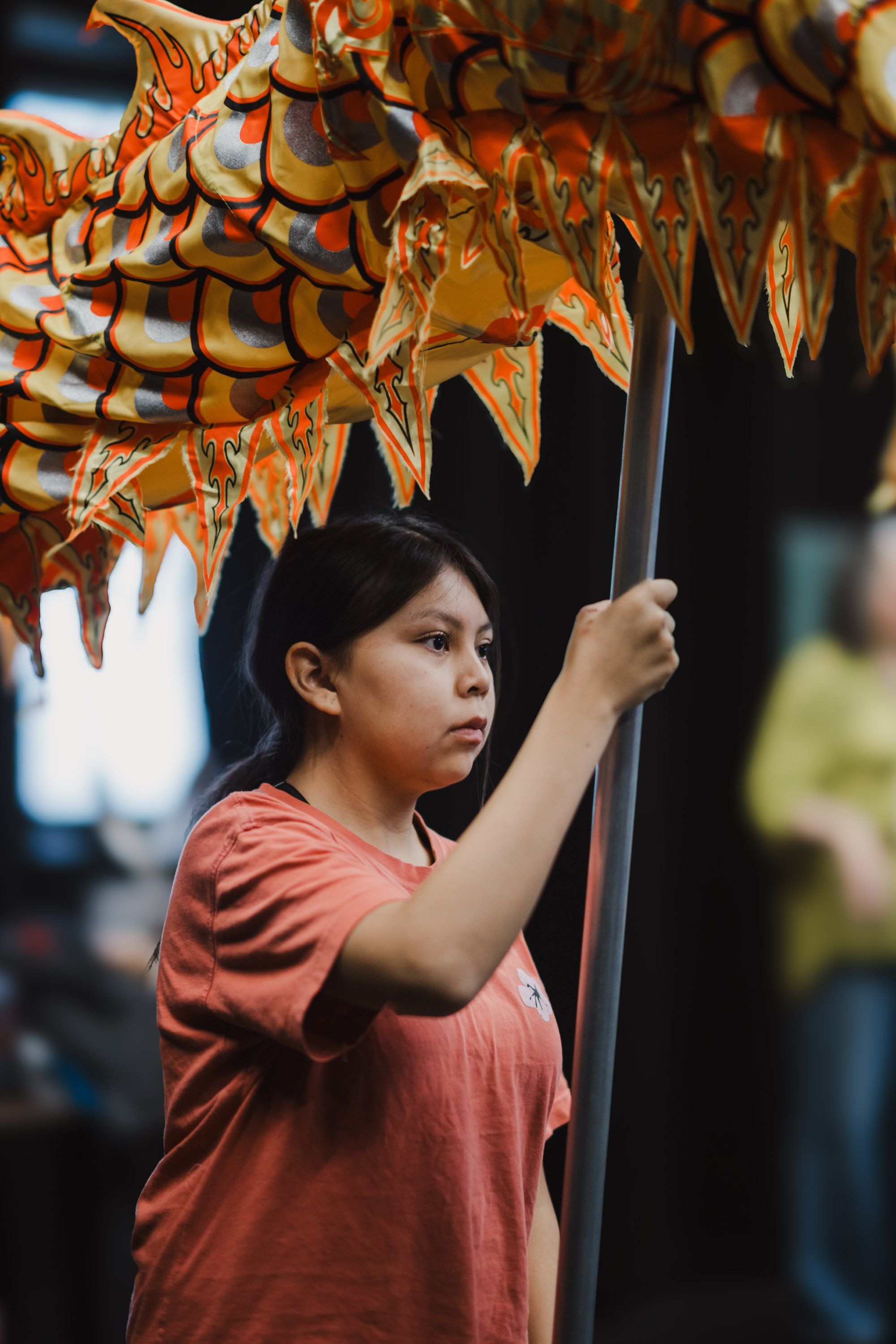 Young child in coral shirt holds pole beneath hanging ornamental fish decorations at cultural celebration