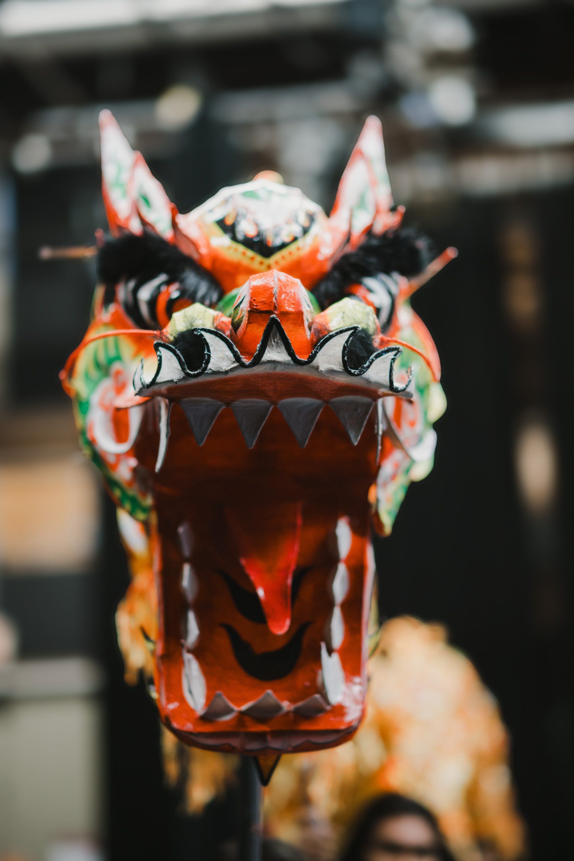 Vibrant red and white carved dragon mask with open mouth and prominent teeth, ornate horns, and detailed artistic patterns displayed outdoors