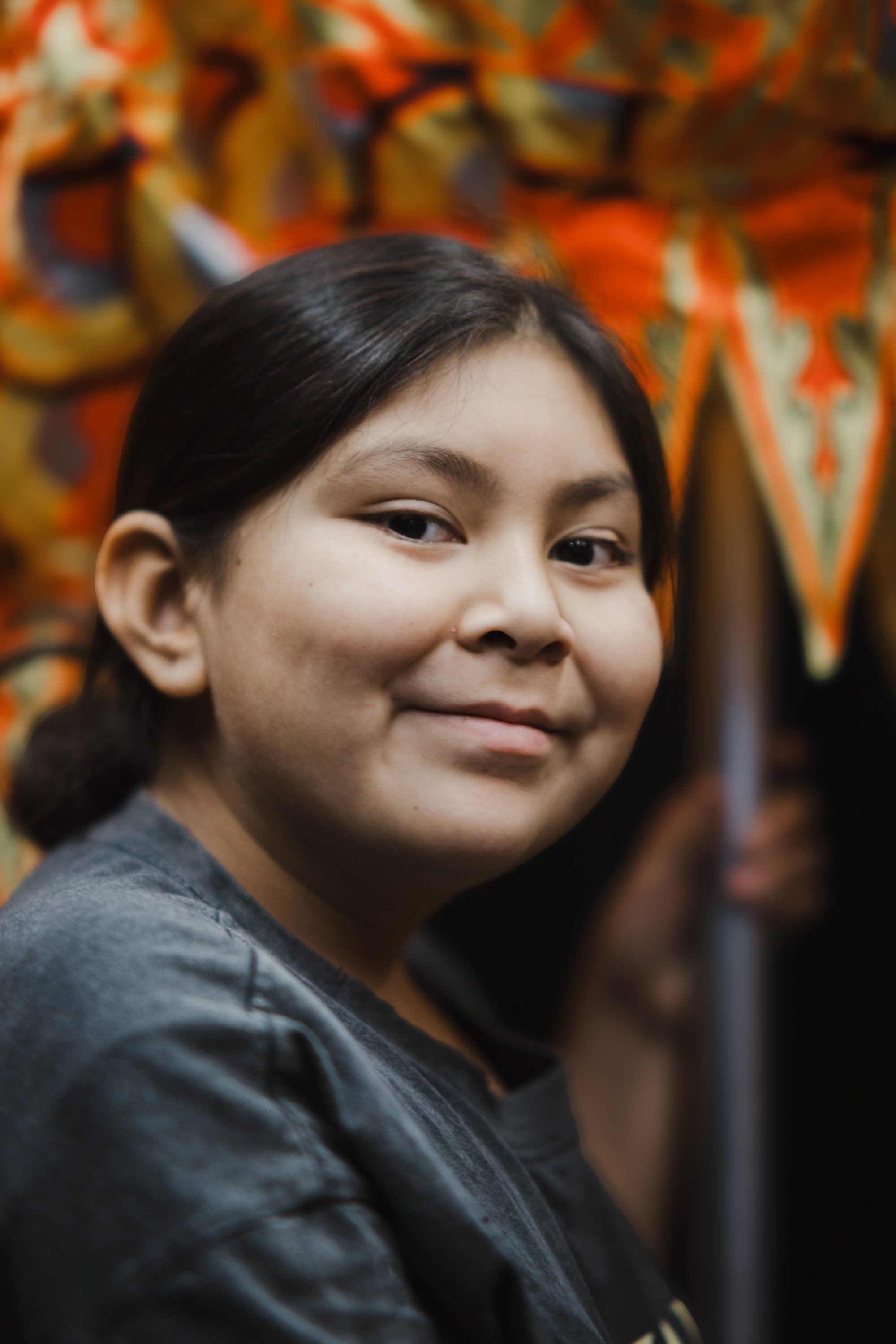 Young woman with long dark hair smiling gently at camera, warm golden and orange tones glowing softly in blurred background