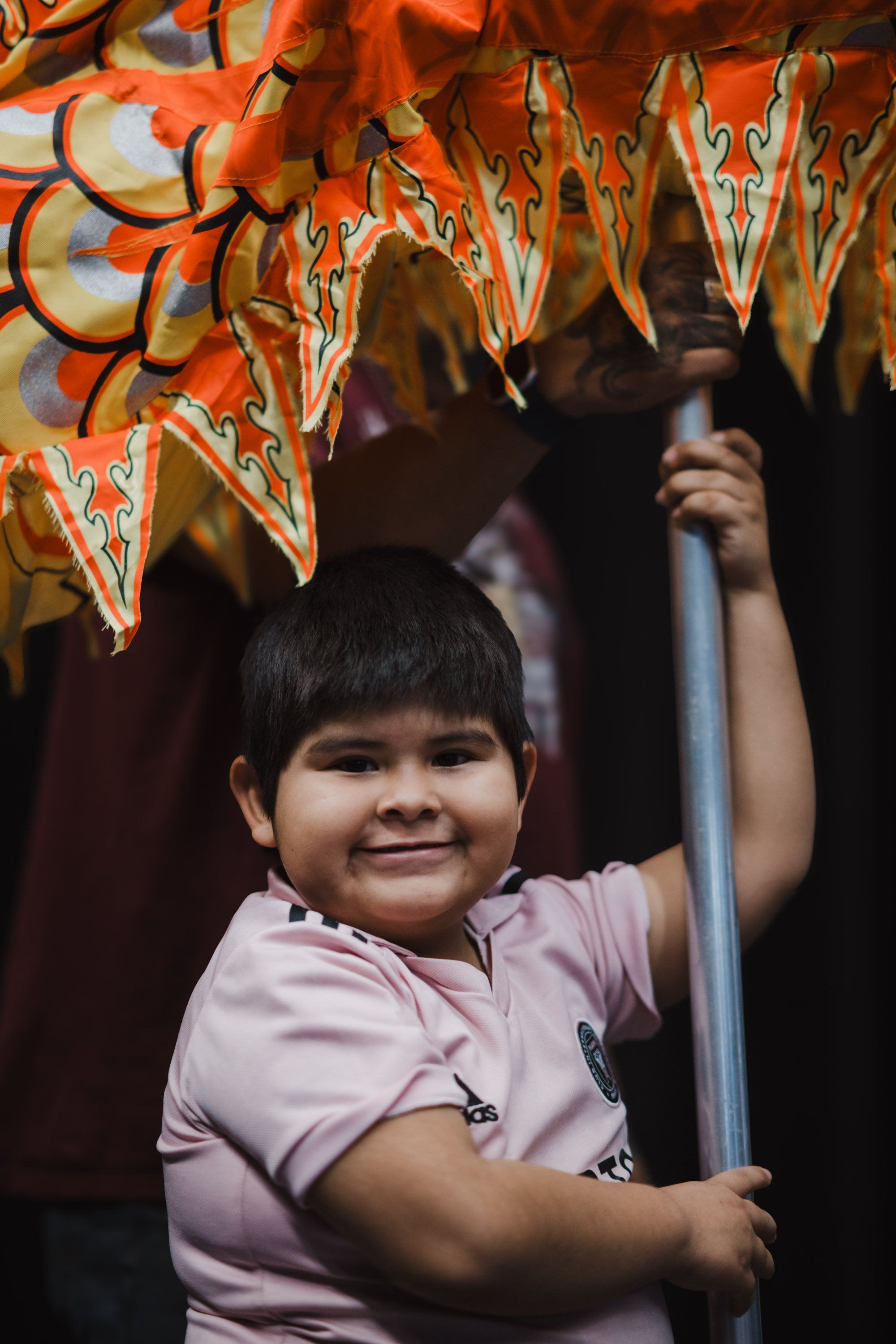 Young child in pink shirt smiling while holding up a decorated orange mask at a Coast Salish cultural celebration