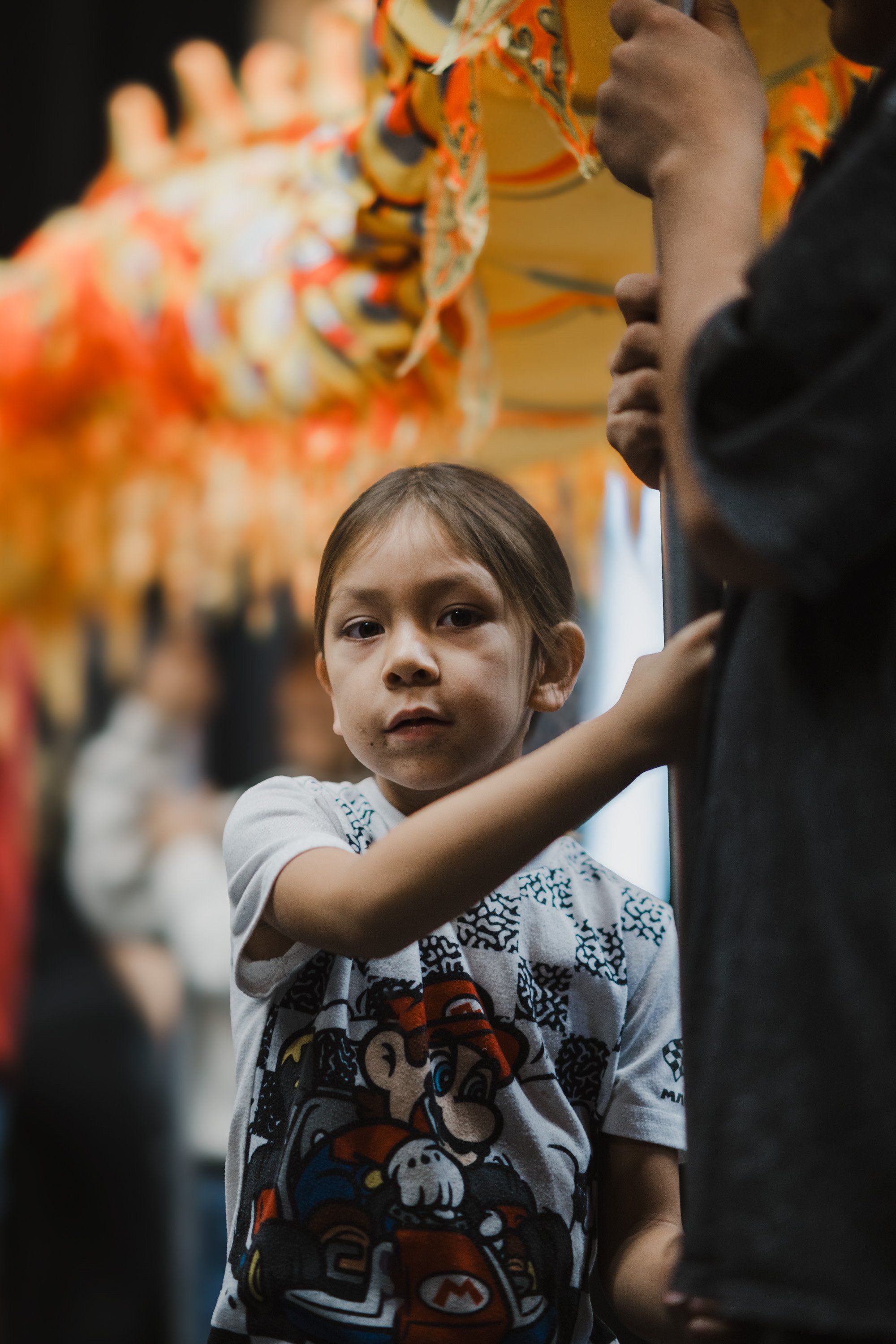 Young child in white graphic tee gazes thoughtfully while holding an ornate golden ceremonial object at a Coast Salish gathering