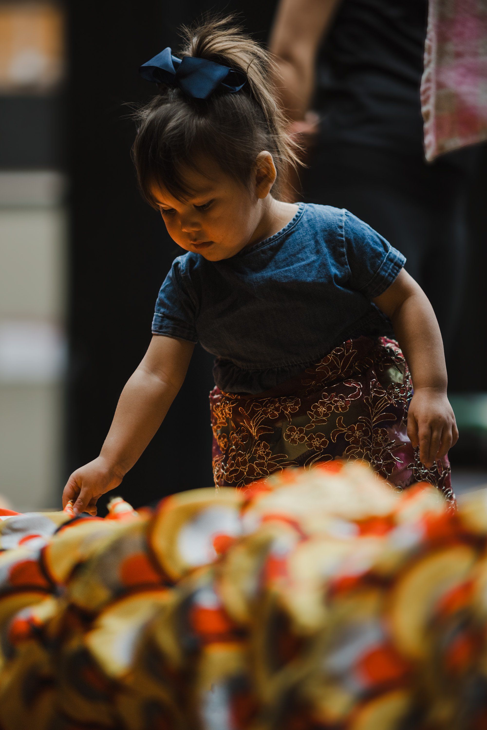 Young girl with blue hair bow concentrating on beadwork, warm golden light illuminating her focused expression