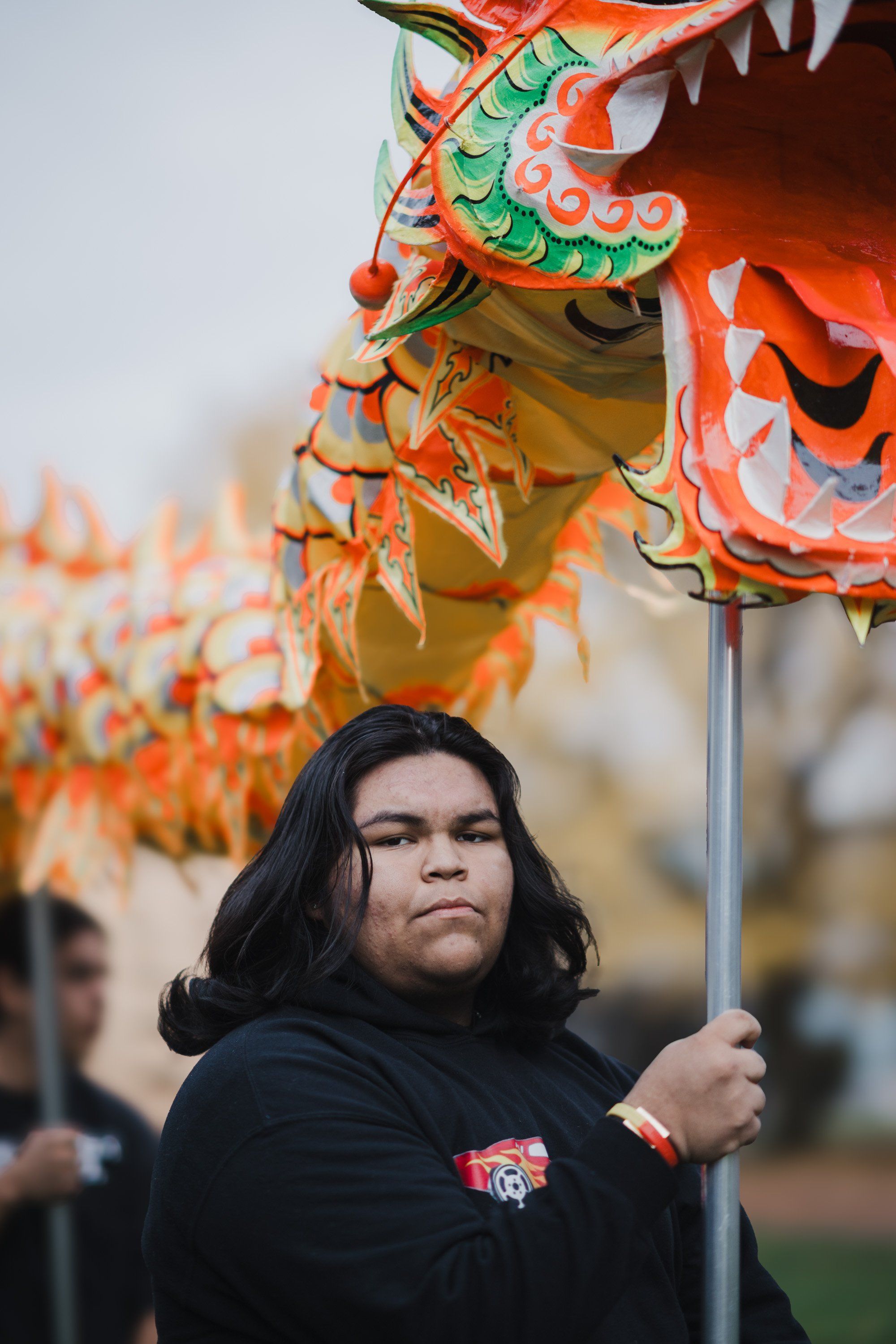 Young person holding an ornate red and green dragon puppet, gazing upward with focused expression during an outdoor cultural celebration