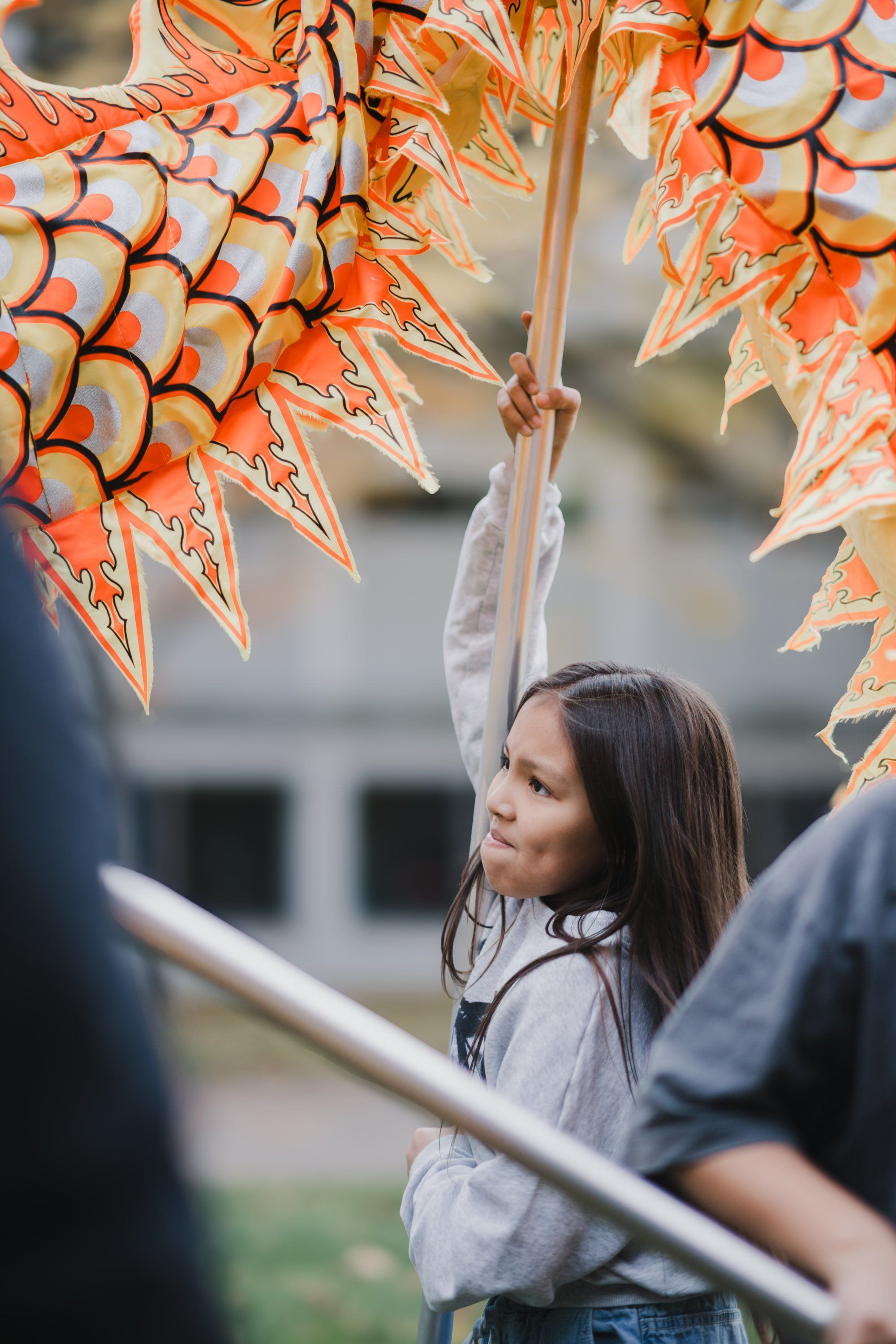 Young person reaching up toward hanging decorative fish amid golden autumn light at a Coast Salish celebration