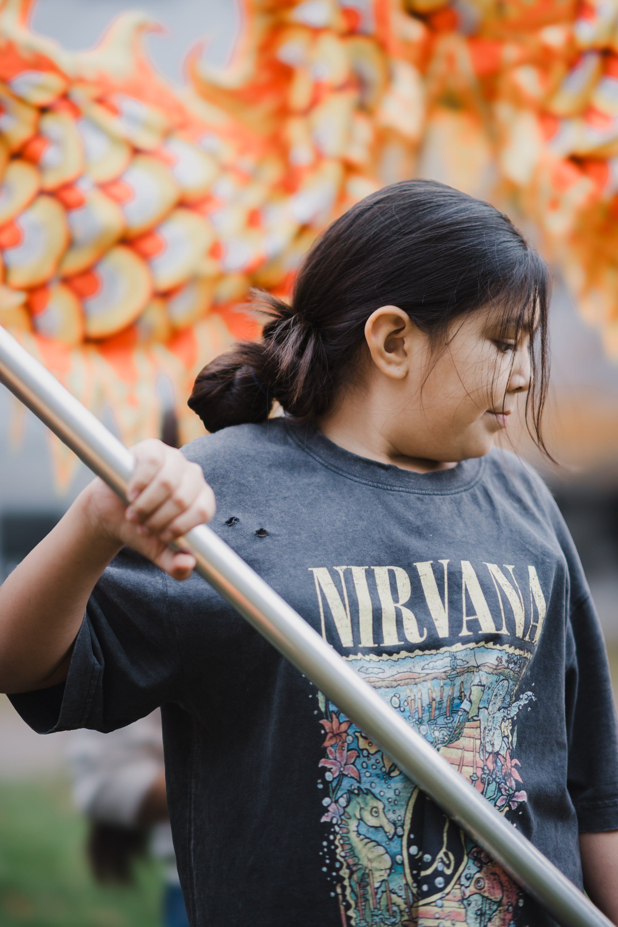 Young person in Nirvana band tee holds wooden pole, golden autumn foliage glowing behind them
