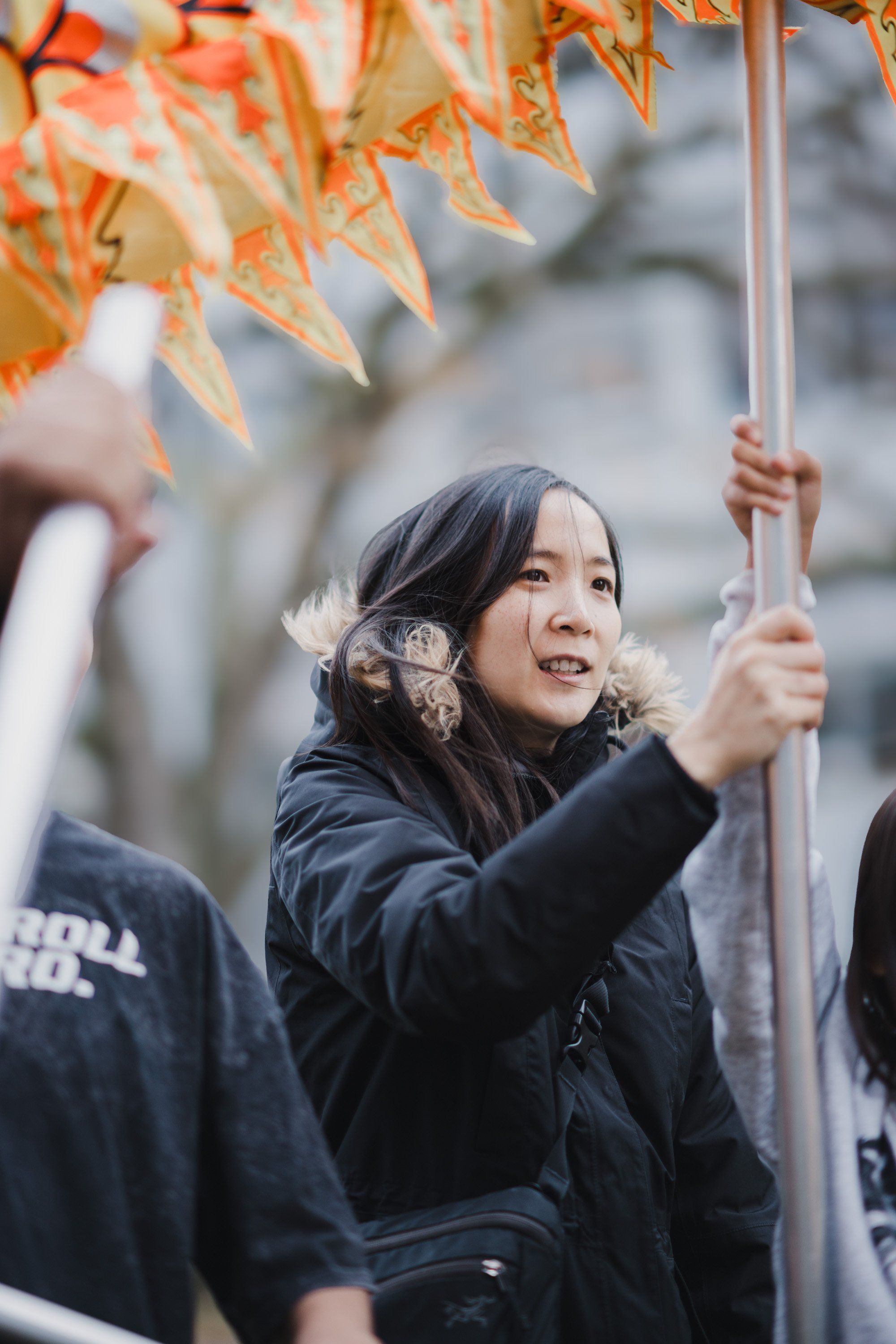 Young woman in dark jacket reaches up to touch golden autumn leaves, smiling with joy during a celebration of Coast Salish culture