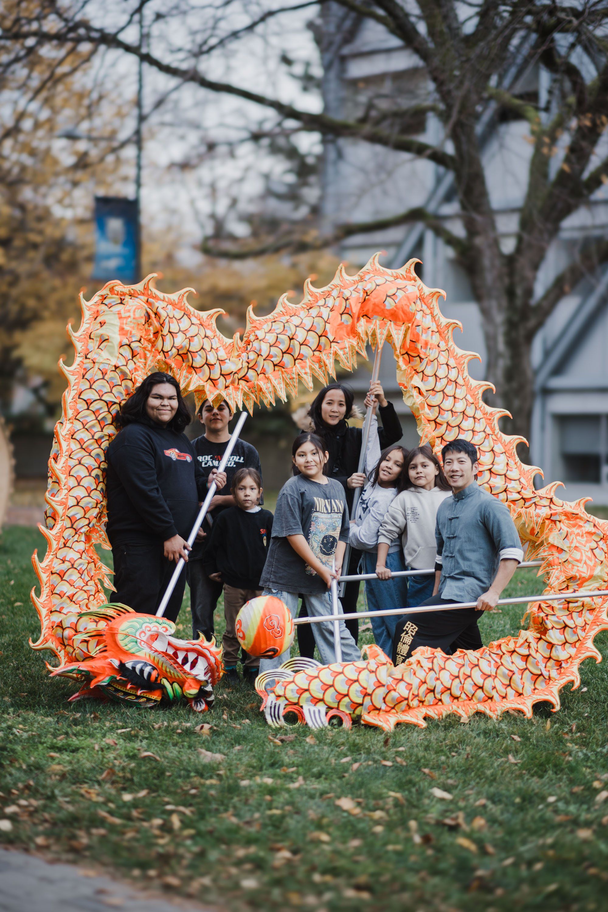 Large group of children and adults posed within an orange pumpkin-shaped frame made of smaller pumpkins, smiling at camera on grass