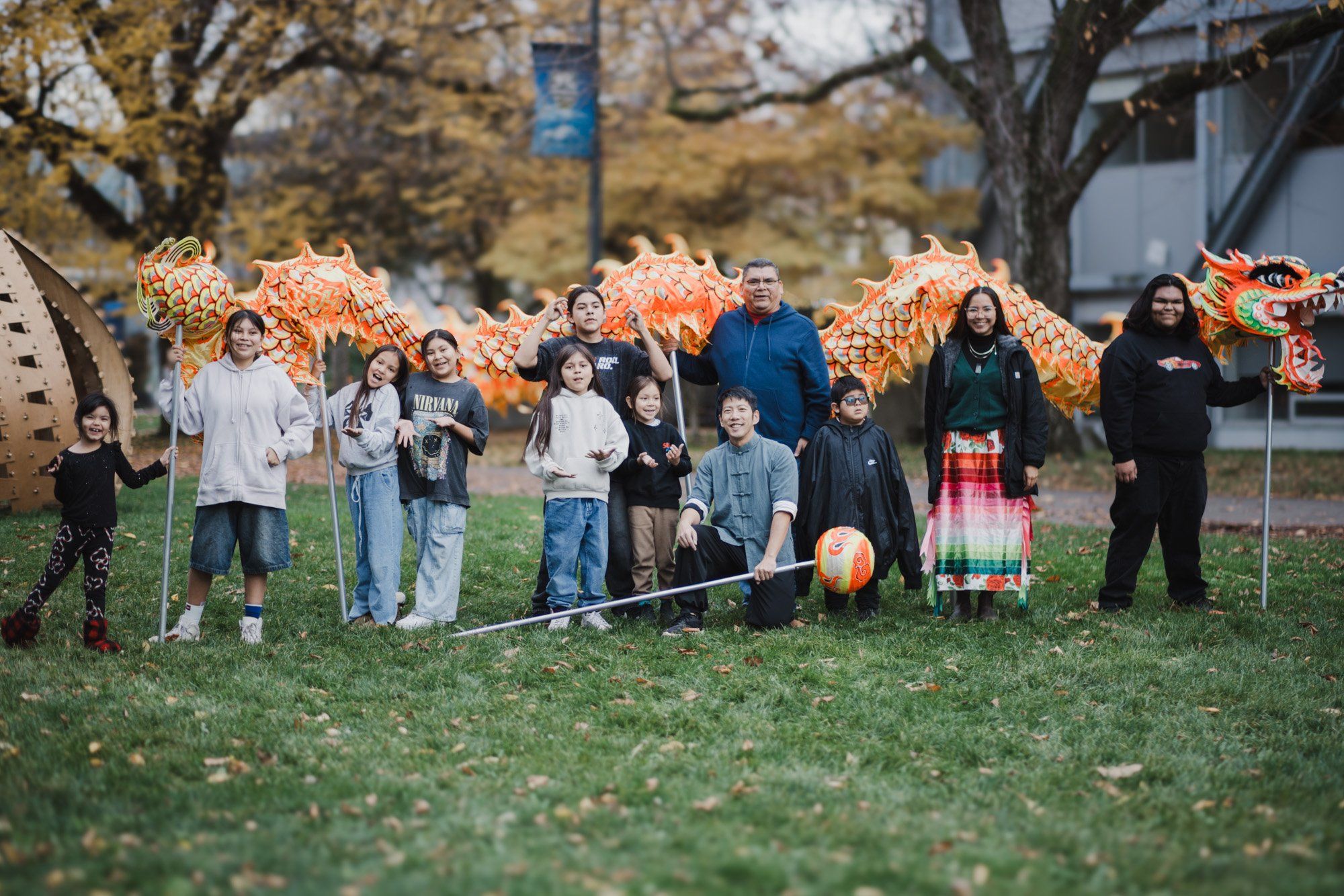 Group of people standing together on a grass field with large orange decorative wolves behind them, autumn trees and buildings visible in background
