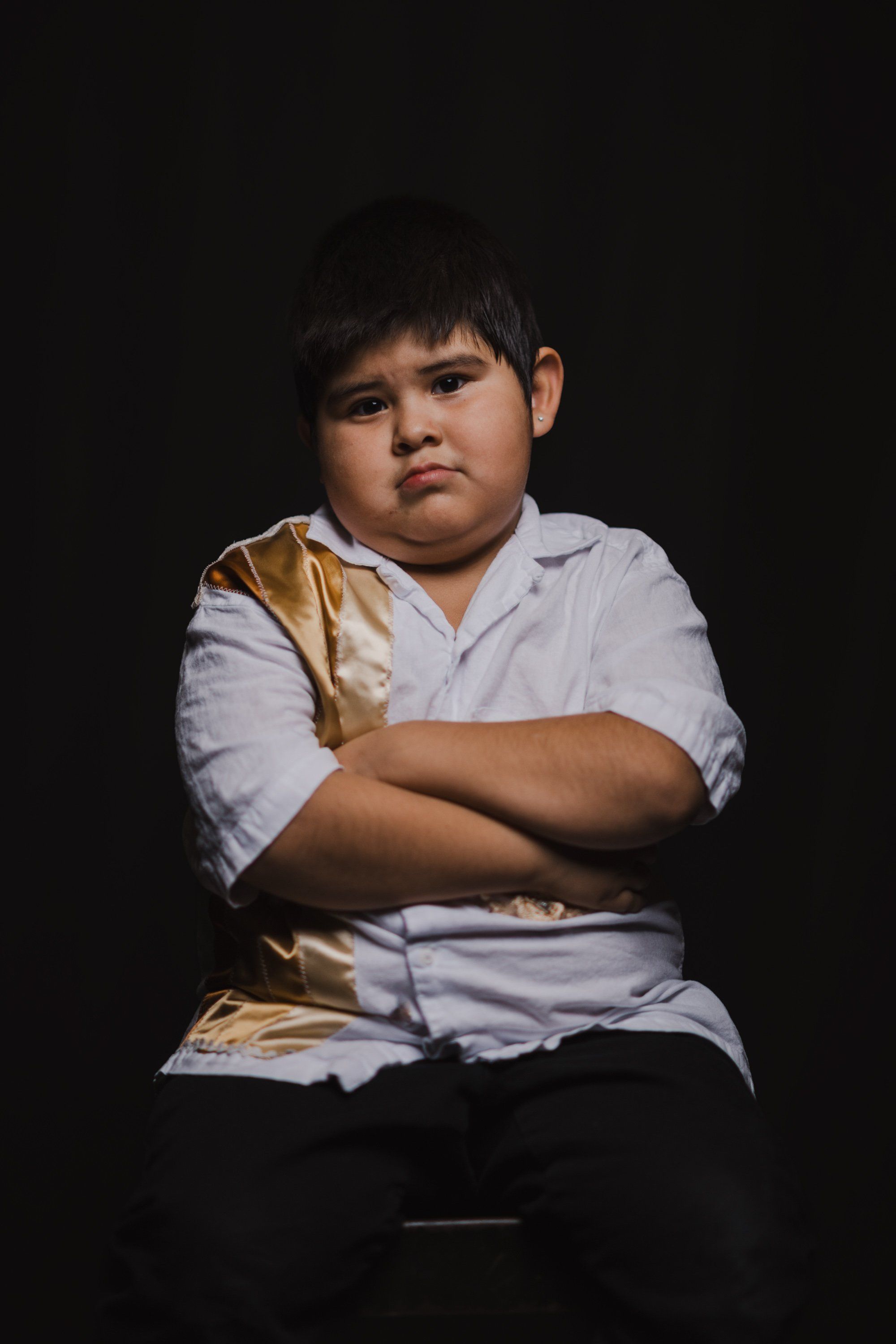 Young person in white button-up shirt with arms crossed, serious expression, dramatically lit against dark background
