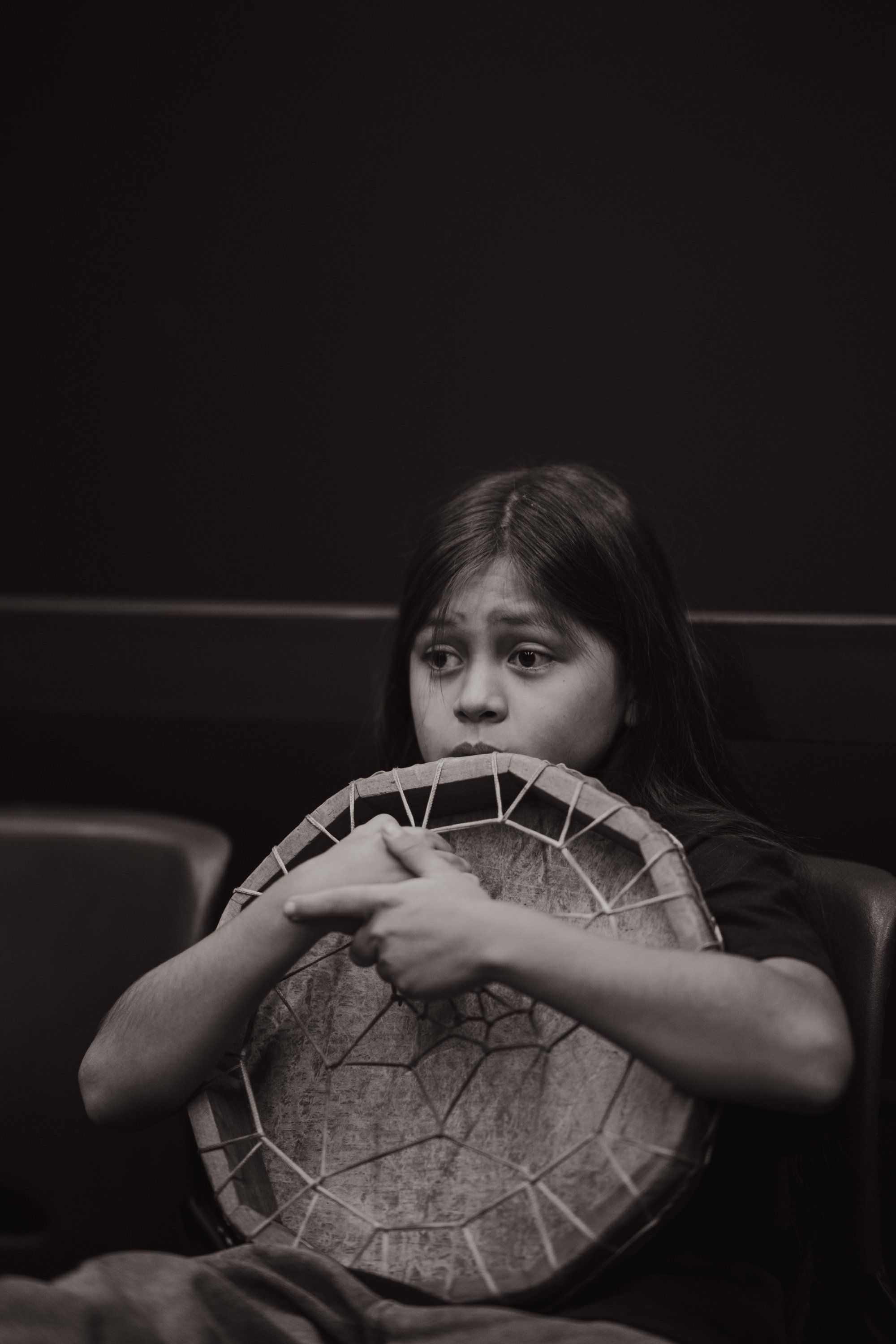 Young girl holding a woven basket, gazing directly at camera in black and white portrait against dark background
