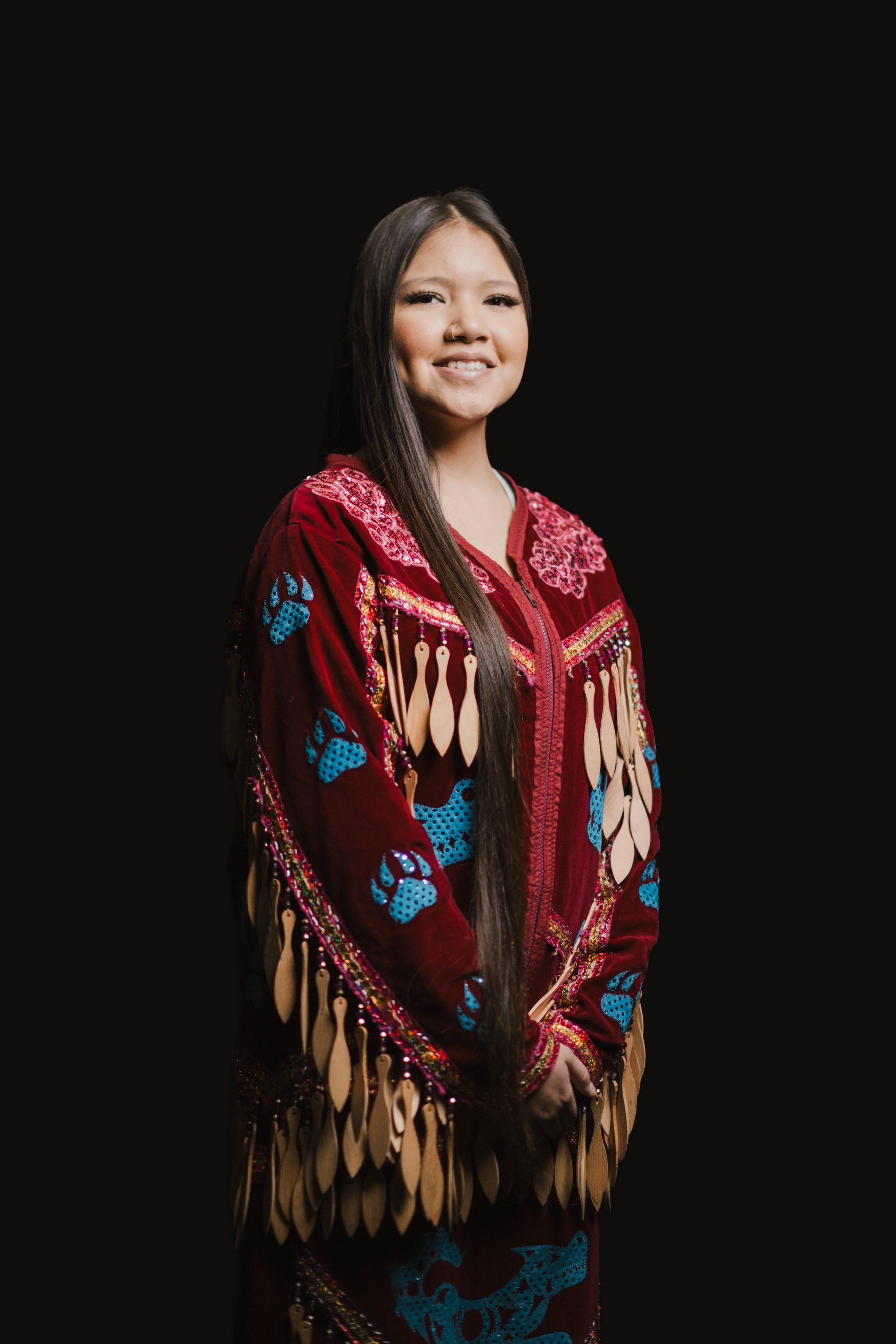 Woman in deep red wool shawl with blue and cream geometric patterns and long fringe, smiling against black background