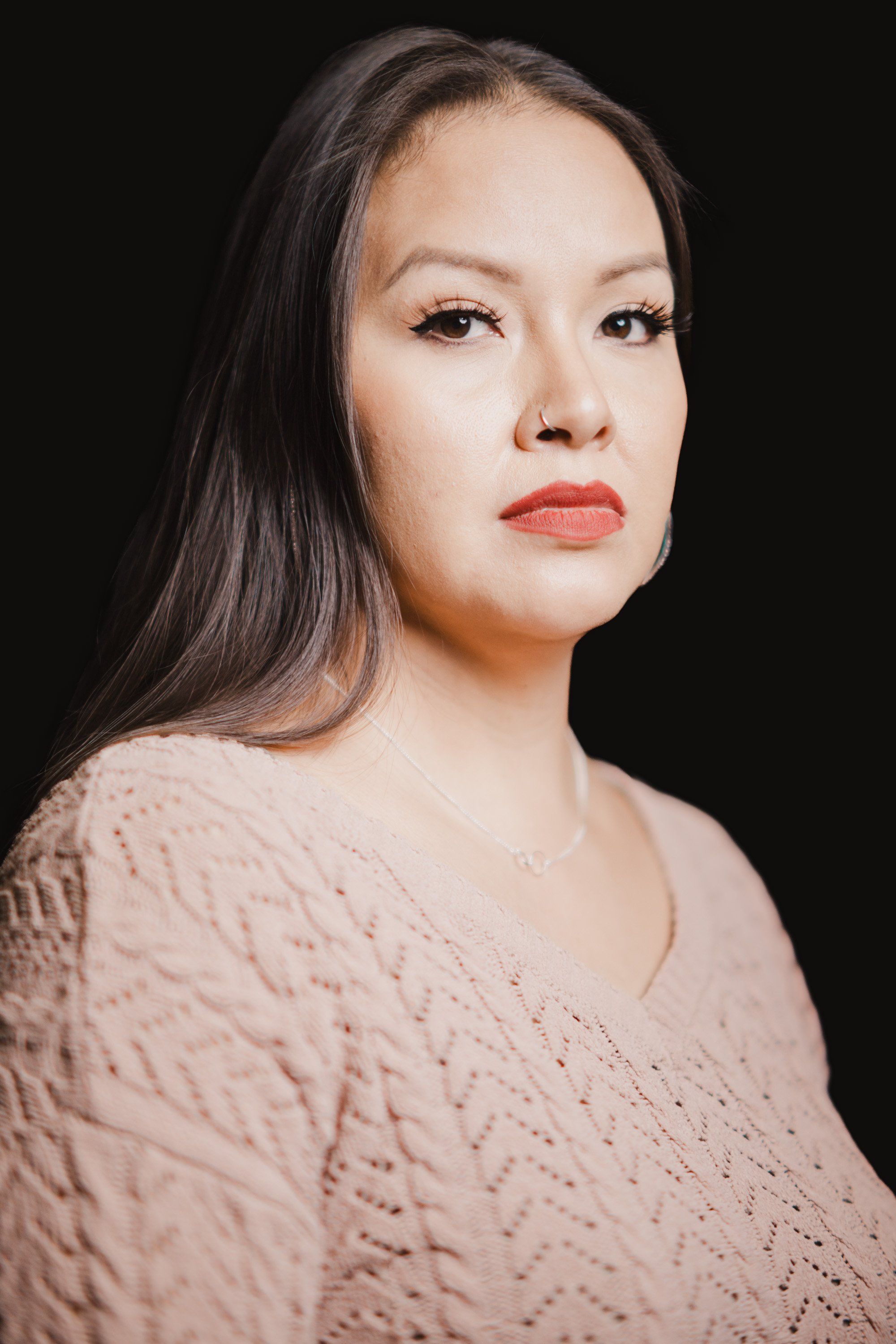 Woman in a textured cream sweater gazes thoughtfully to the side against a black background, warm studio lighting illuminating her face