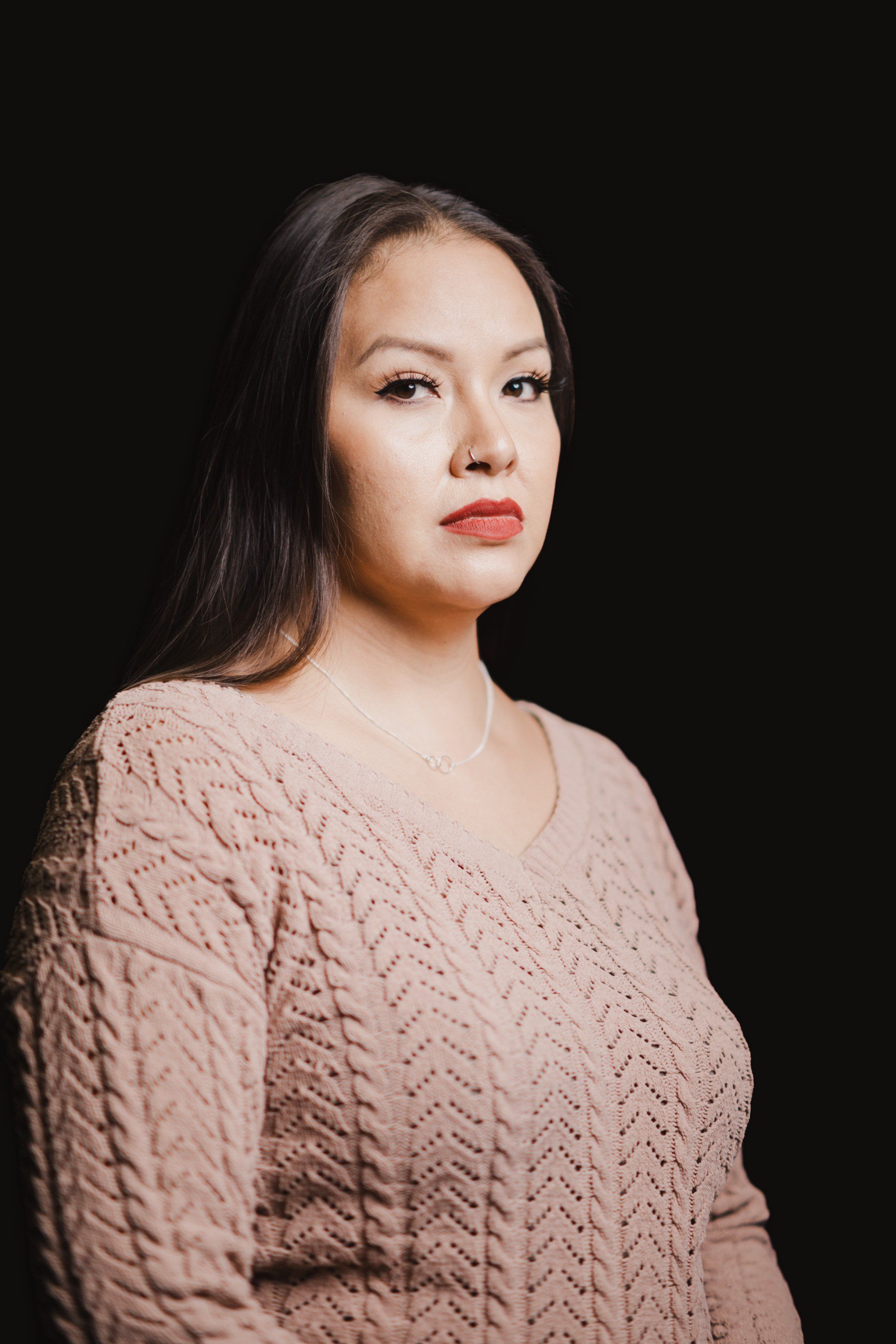 Woman in a textured beige cable-knit sweater gazes thoughtfully to the side against a black background