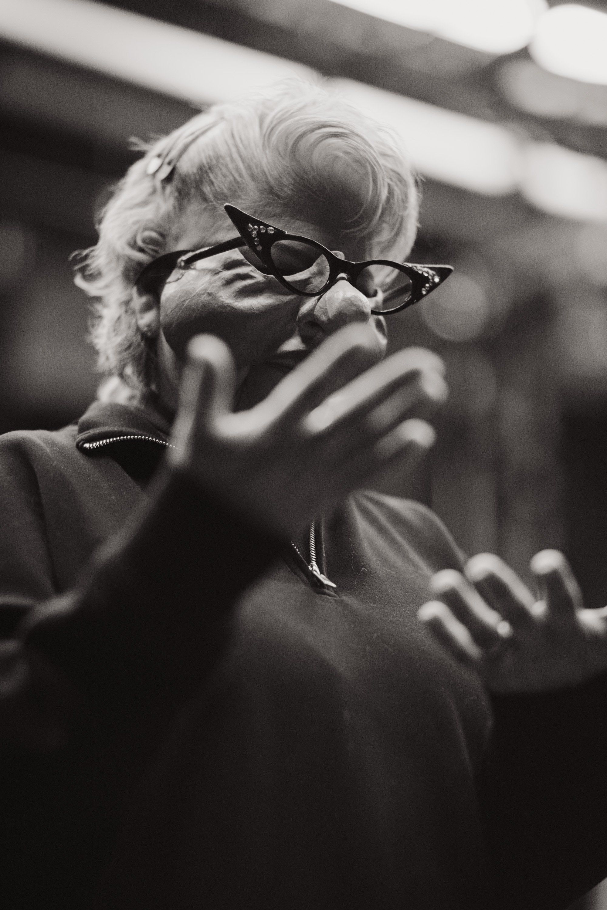 Elder with white hair and glasses gestures expressively during a performance, captured in intimate black and white portrait