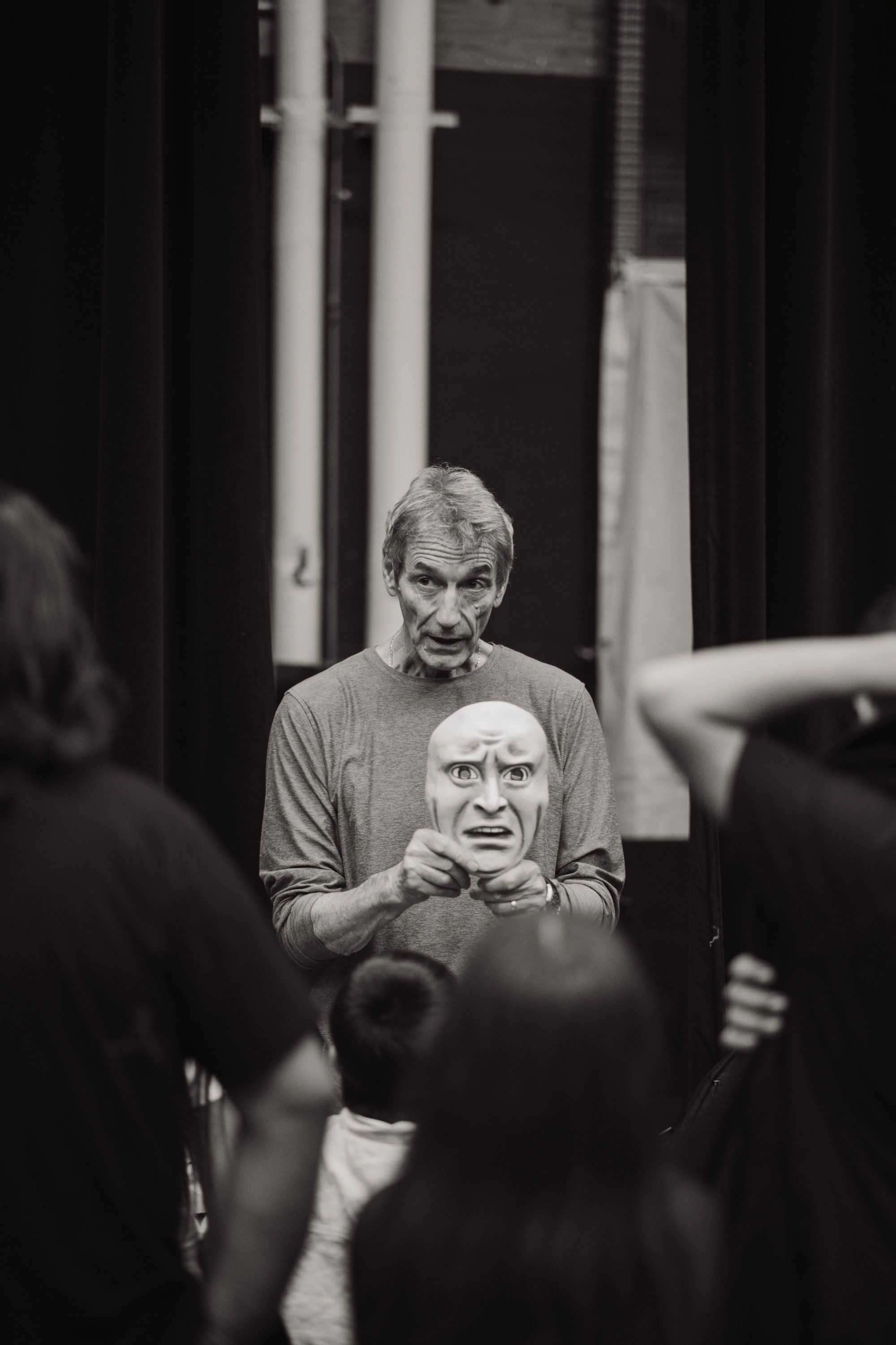 Man holding carved mask faces audience in intimate black-and-white performance moment, showcasing Coast Salish artistry and cultural expression