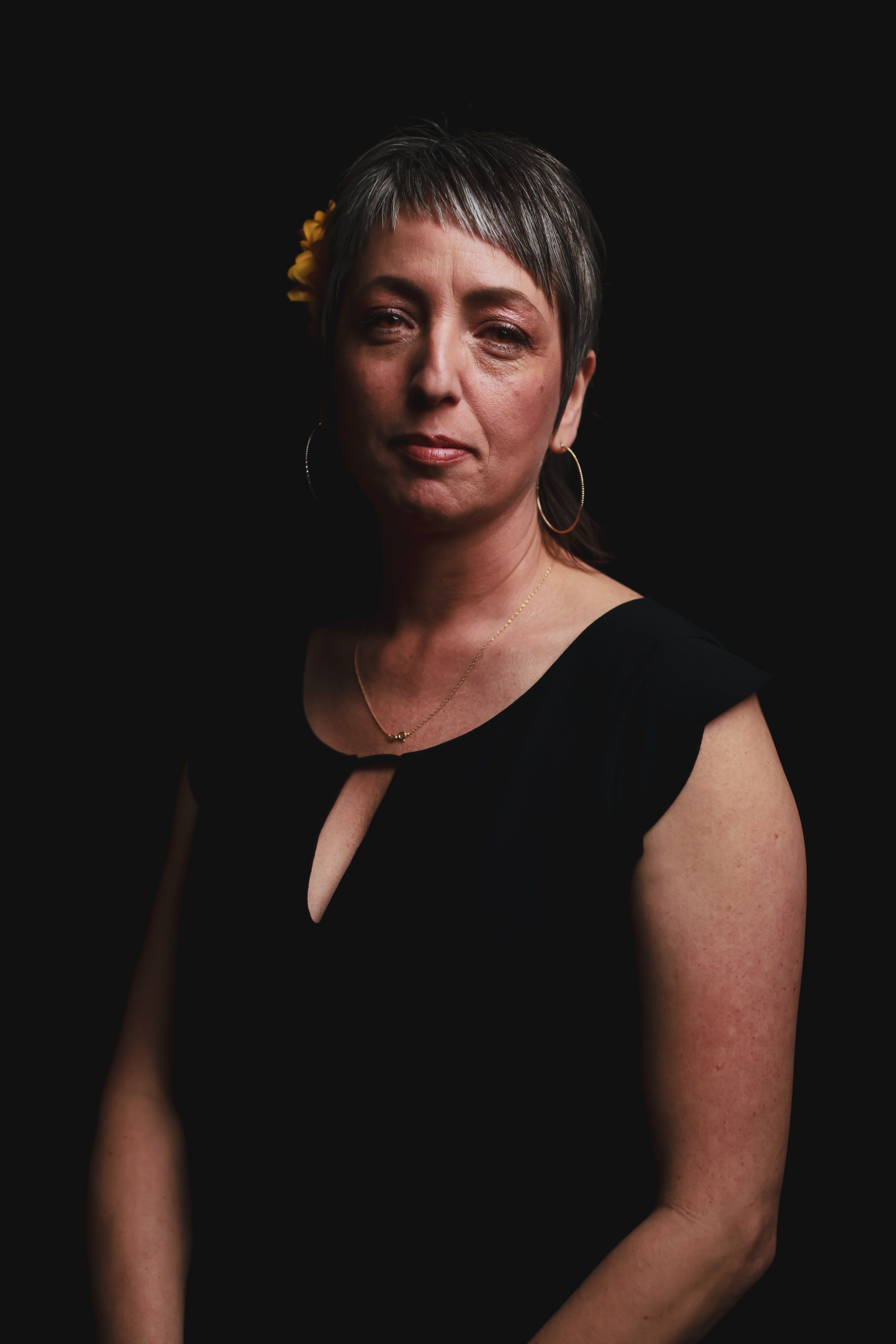 Woman with short dark hair wearing a black sleeveless top against a dark background, warmly lit from the side