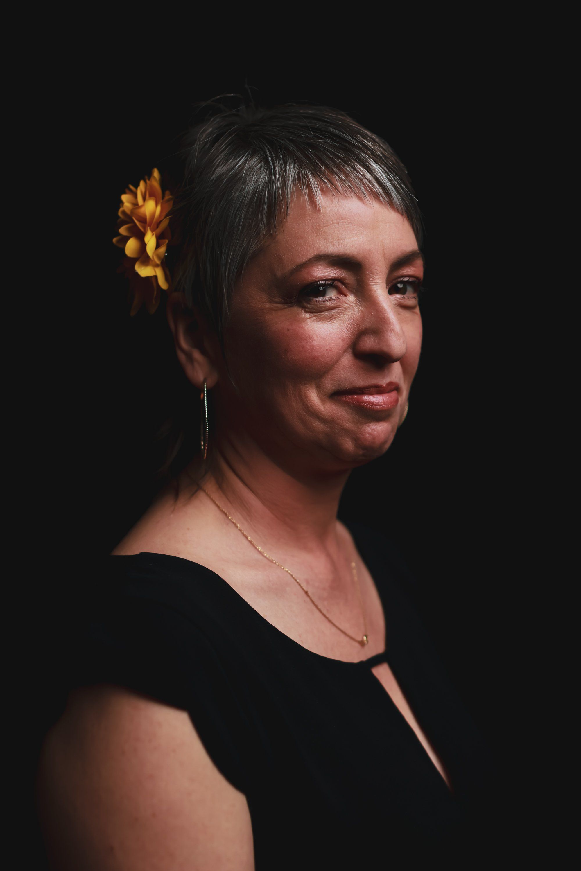 Woman in black top with golden flower hair ornament, profile against dark background, warm studio lighting