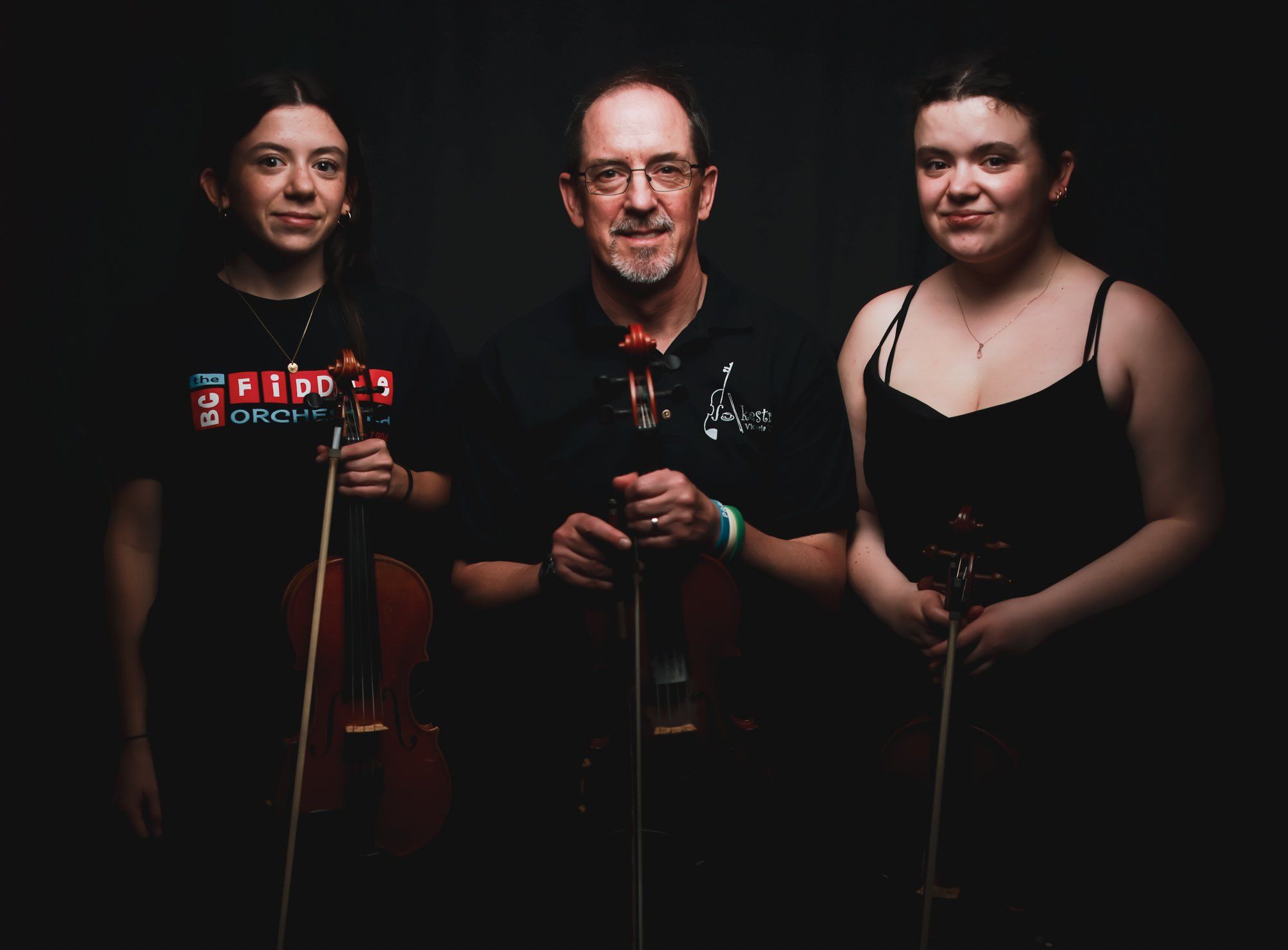 Three musicians holding microphones against a dark background, dressed formally for a concert performance