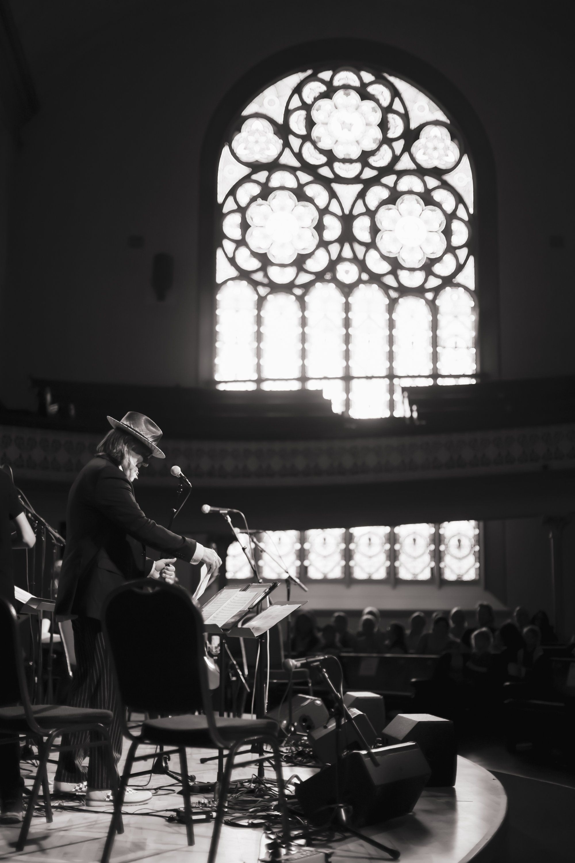 Saxophonist performs in concert hall silhouetted against ornate stained glass window flooding the space with bright light