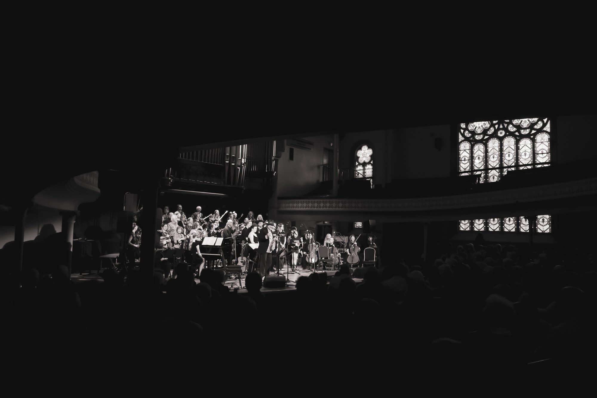 Choir members illuminated on stage in a candlelit church interior, stained glass windows glowing softly in the darkness