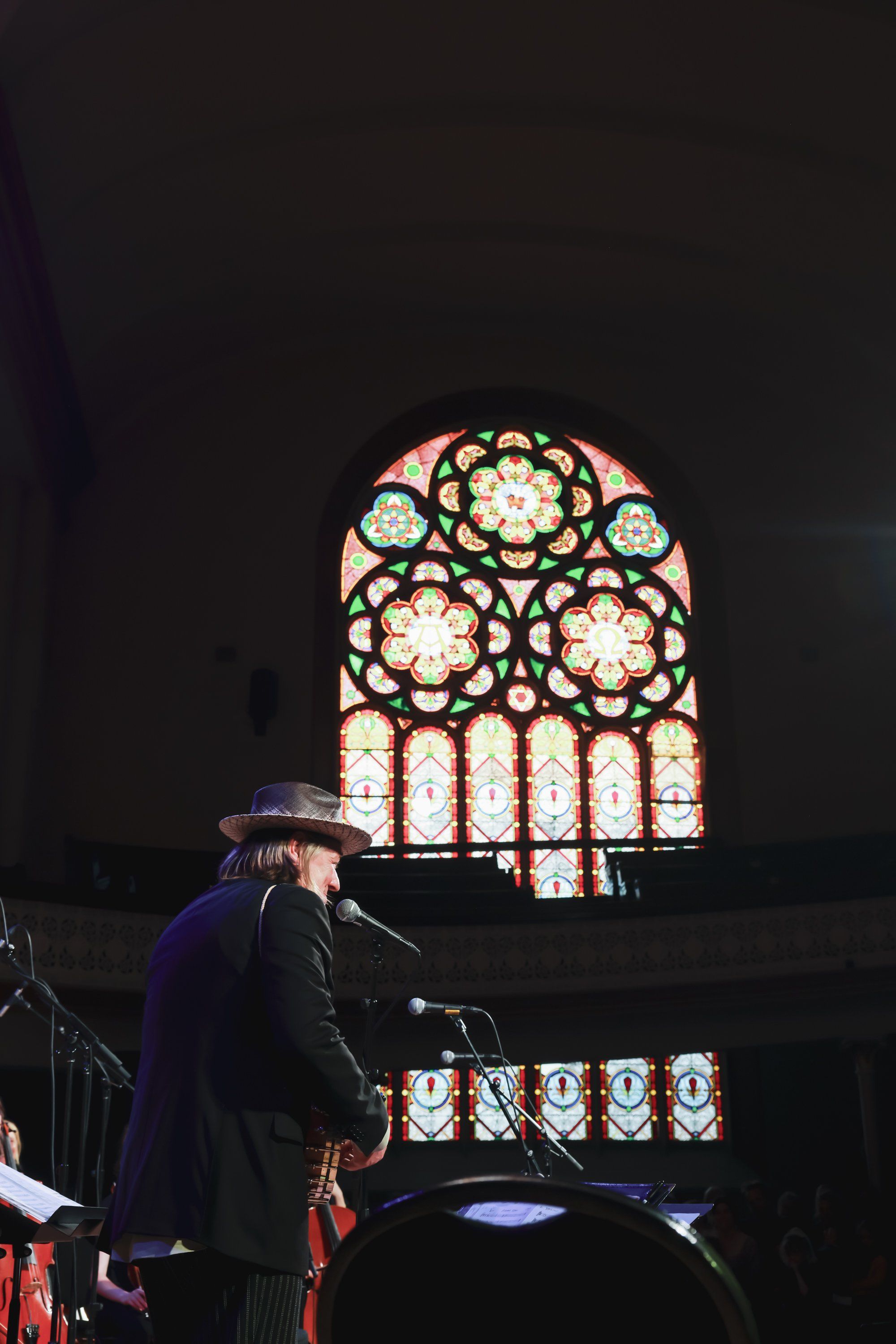 Musician performing at a grand piano beneath an ornate stained-glass window glowing warmly against dark interior walls