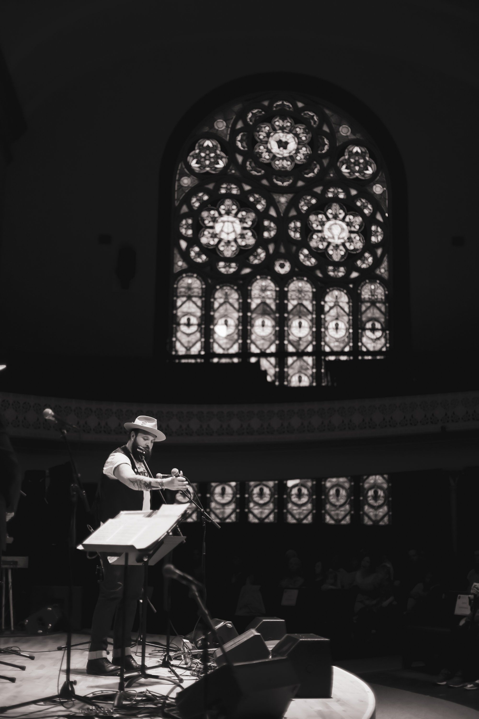 Musician performing solo at grand piano beneath ornate stained-glass window in candlelit cathedral setting