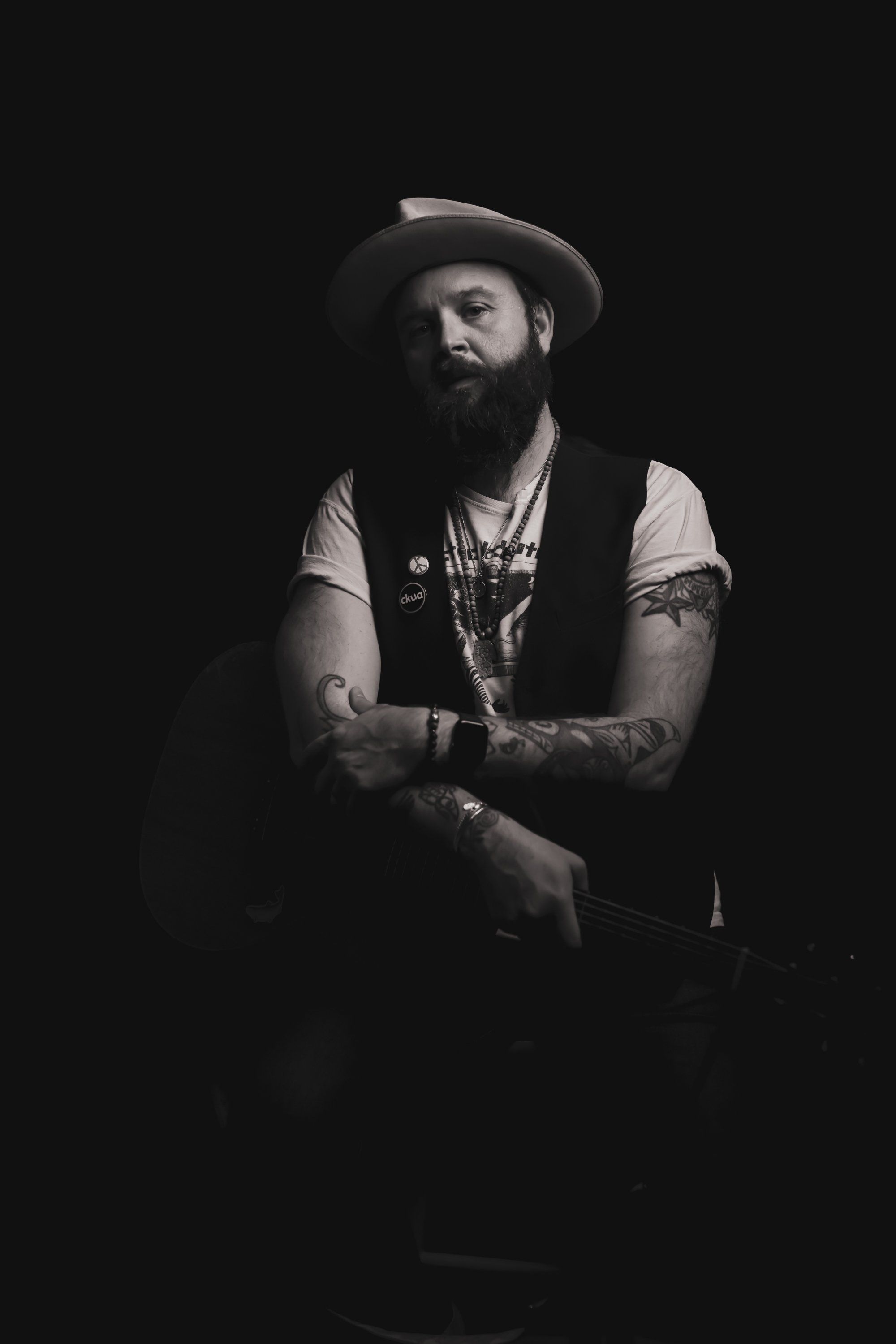 Bearded man in cowboy hat and vest with arms crossed, shot against dark background with dramatic side lighting