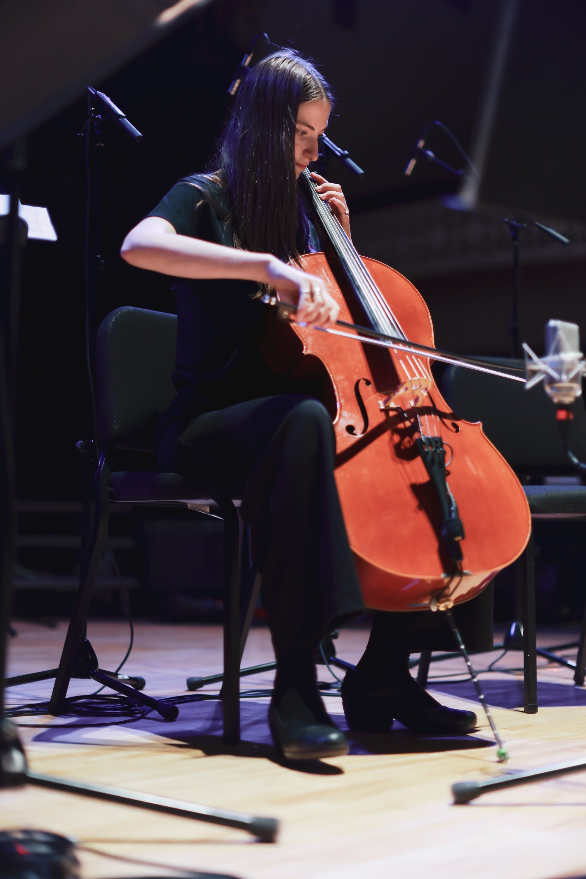 Cellist in black performing with orange instrument under warm stage lighting during concert