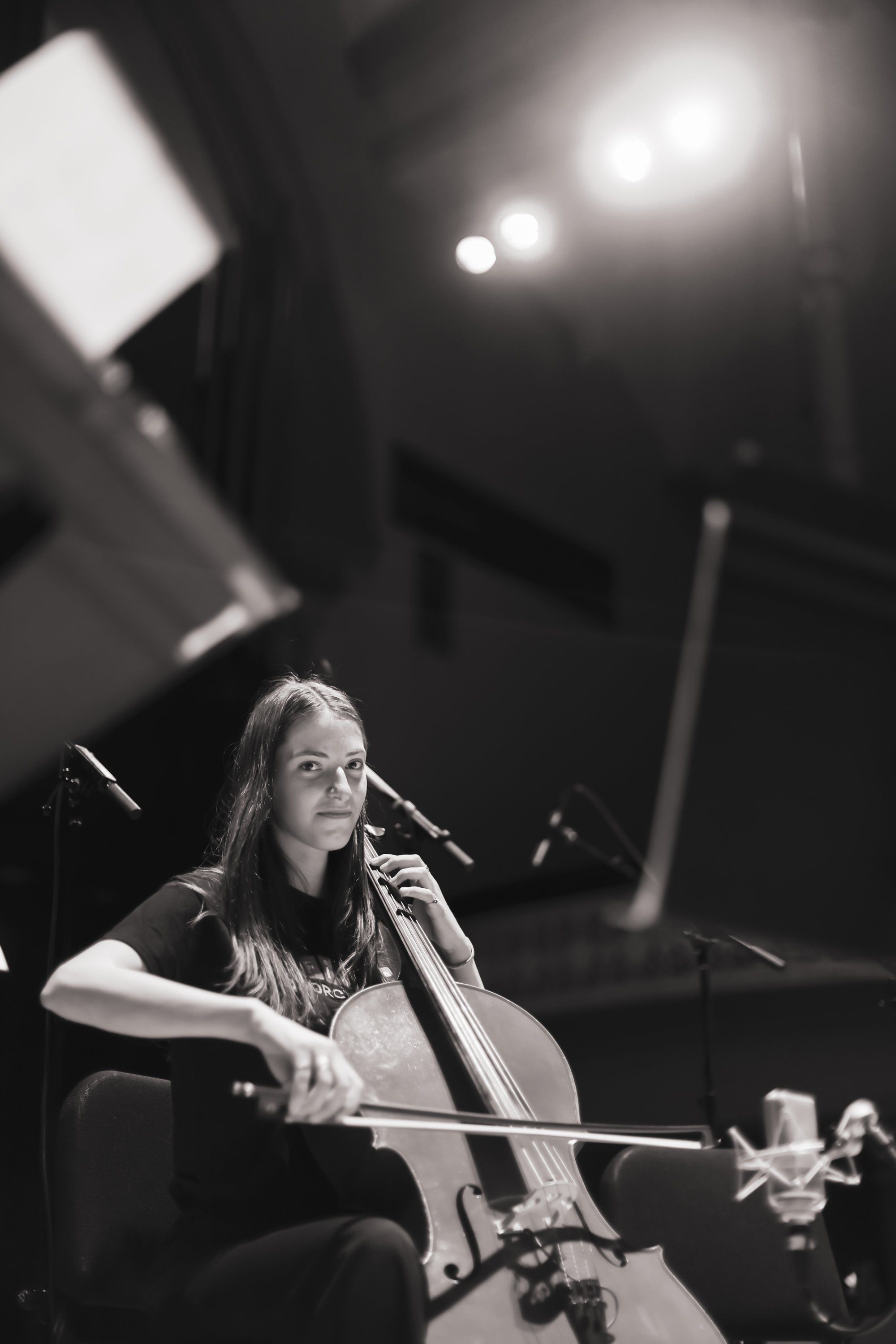 Cellist performing in dramatic stage lighting, long hair falling forward as she focuses intently on her instrument during concert